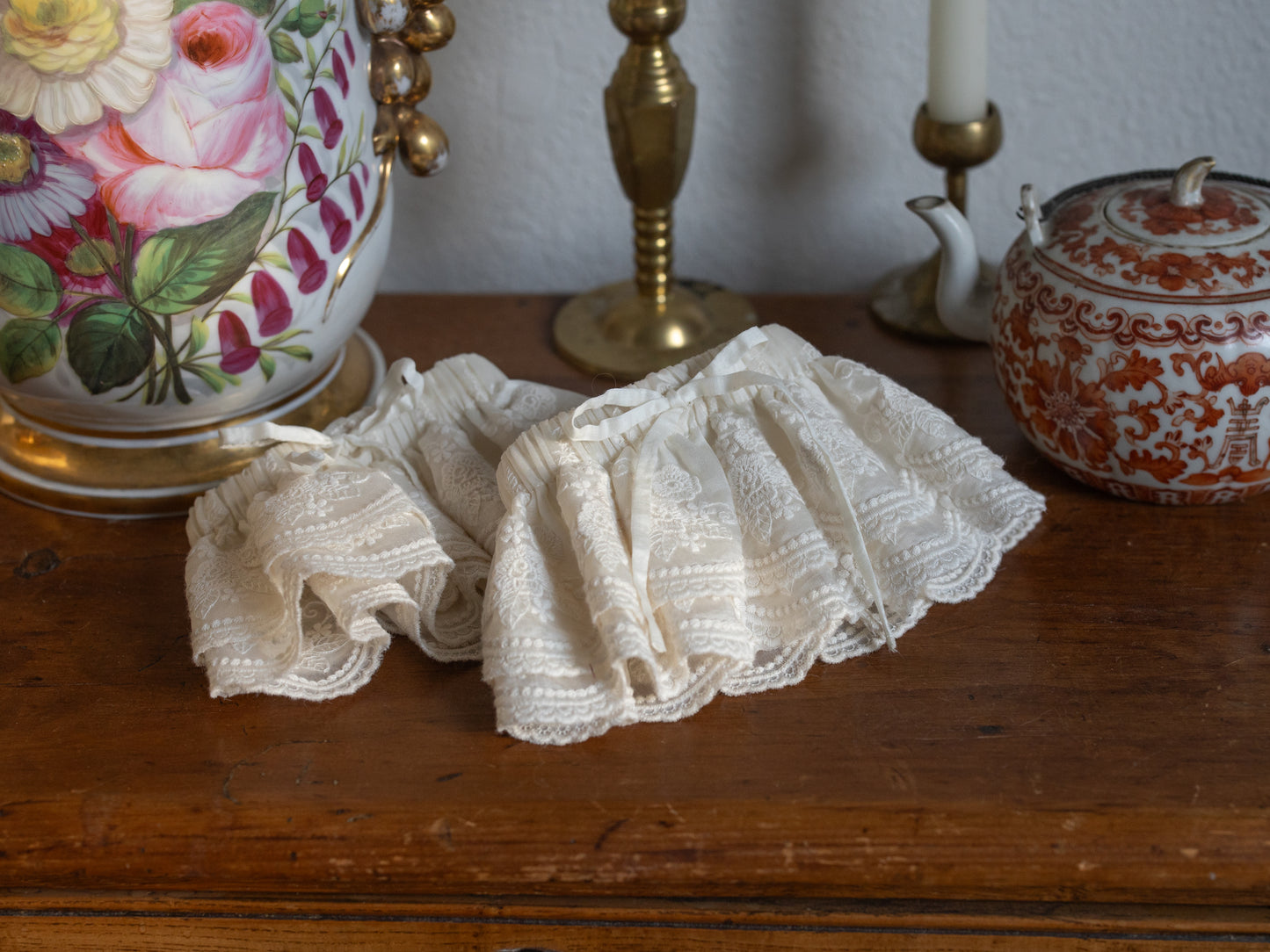 Lacey Ruffle Sleeves displayed on wooden table surrounded by vintage floral vase and brass candlesticks