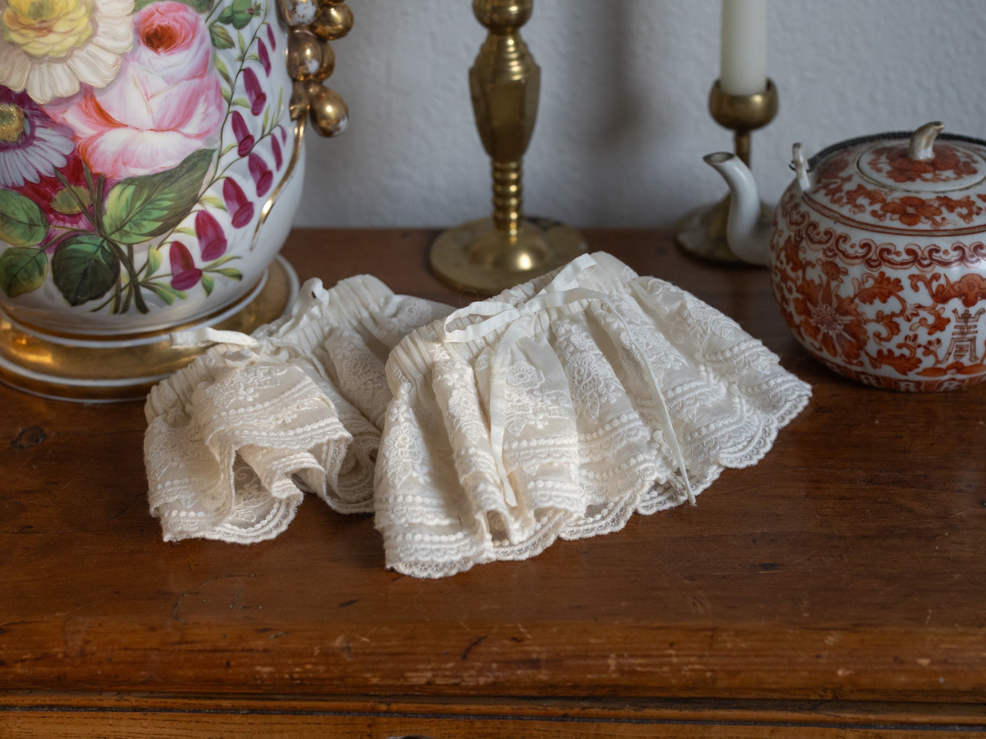 Lacey Ruffle Sleeves displayed on wooden table surrounded by vintage floral vase and brass candlesticks
