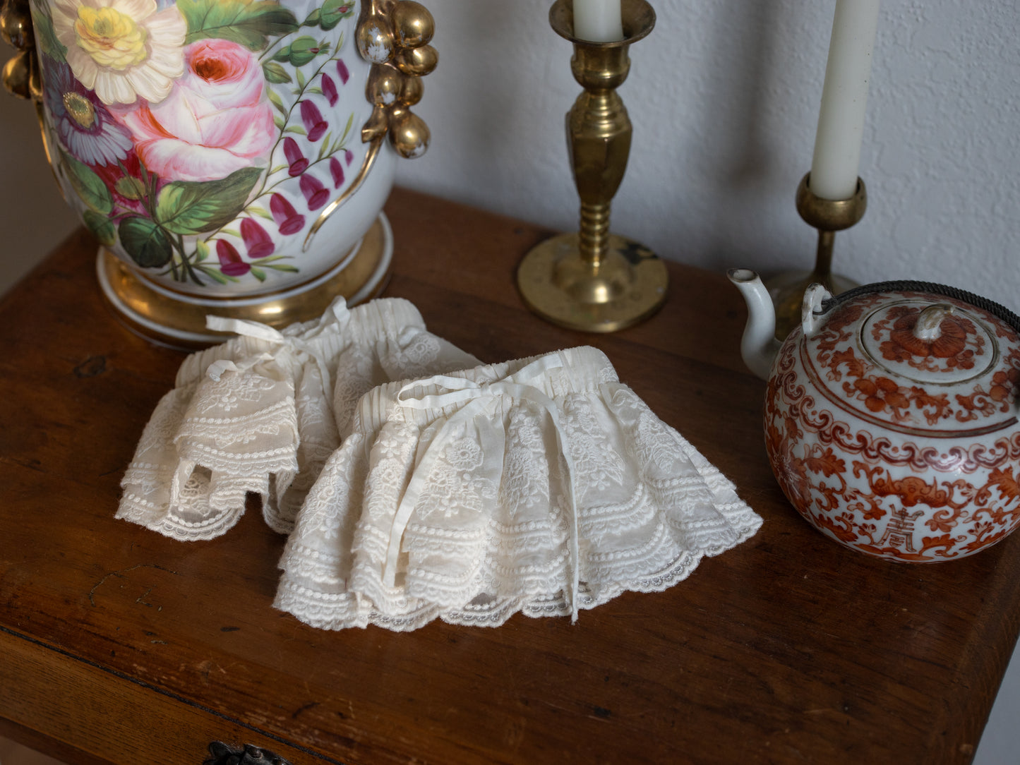 Lacey Ruffle Sleeves in cream lace resting on wooden table with vintage floral vase and candlesticks nearby