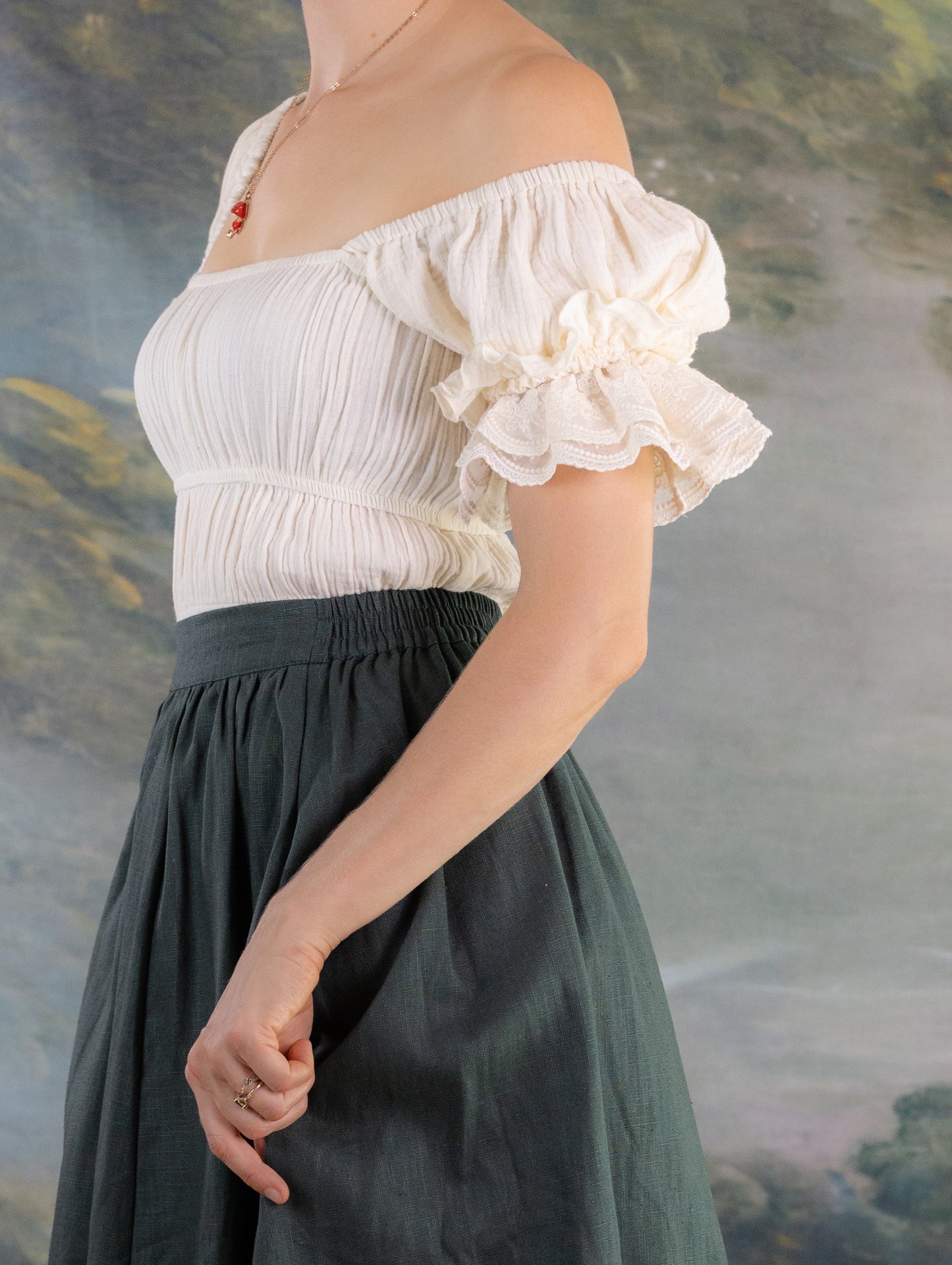 Woman wearing a white off-shoulder top featuring Lacey Ruffle Sleeves and a dark high-waisted skirt against a painted backdrop