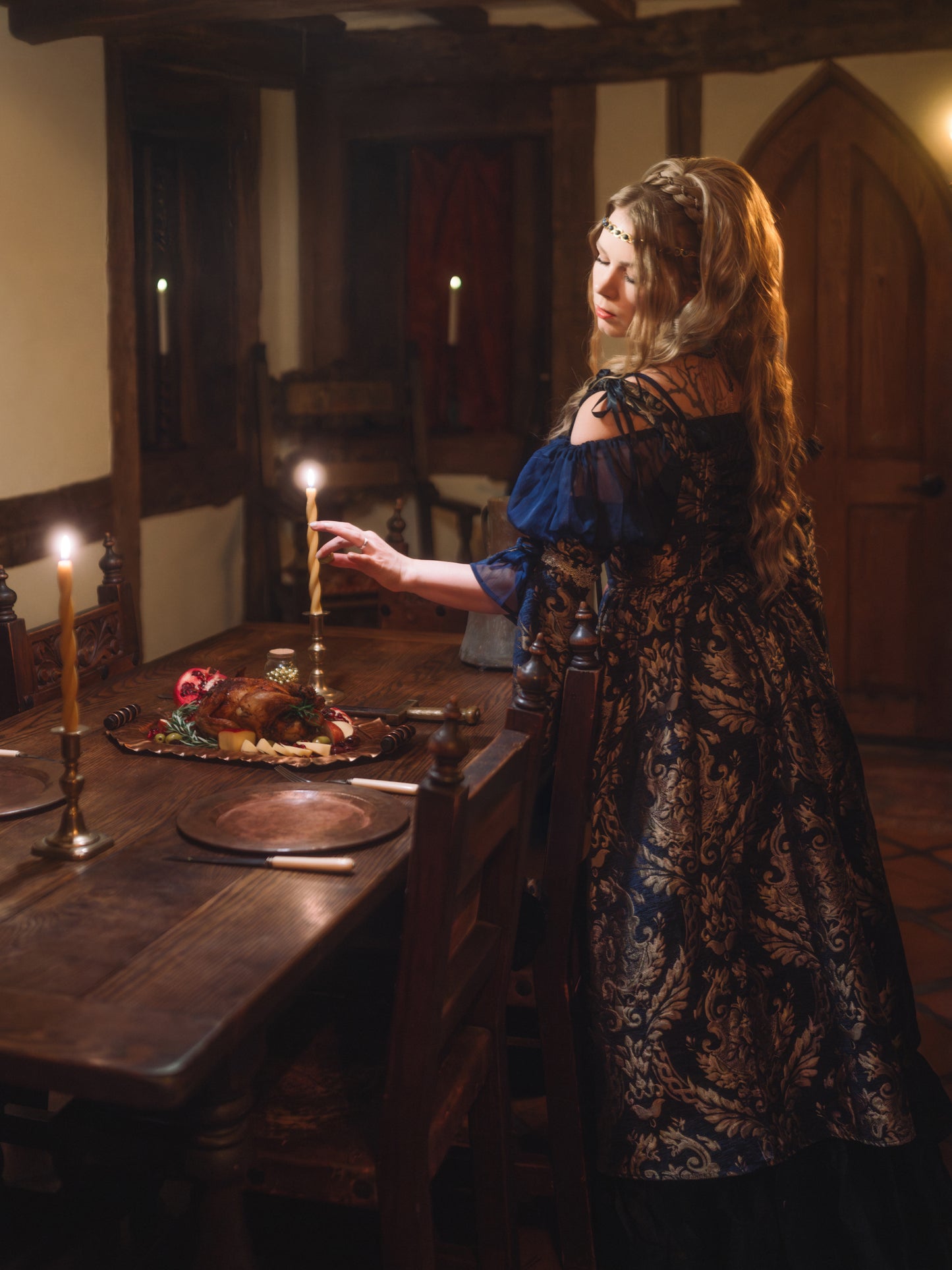 Woman wearing a Navy Blue Chenille Corset Dress lighting candles in a medieval-style wooden dining room