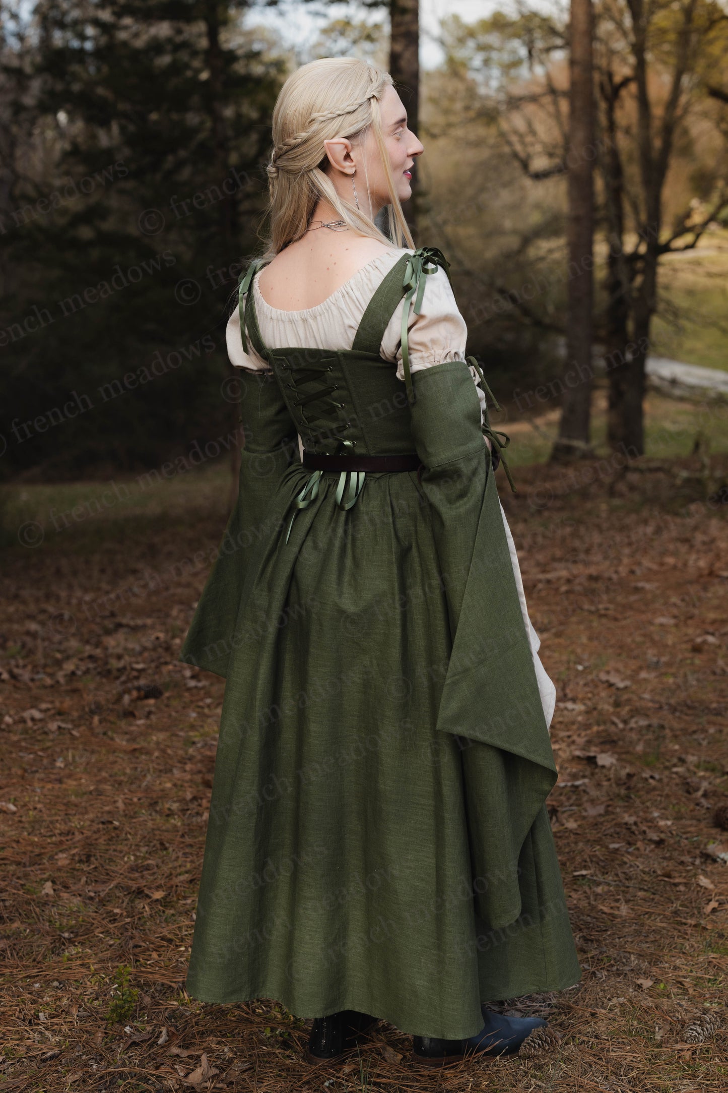 Ivy Green Corset Dress shown from back view in forest setting, featuring laced bodice, flowing skirt and bell sleeves in natural light