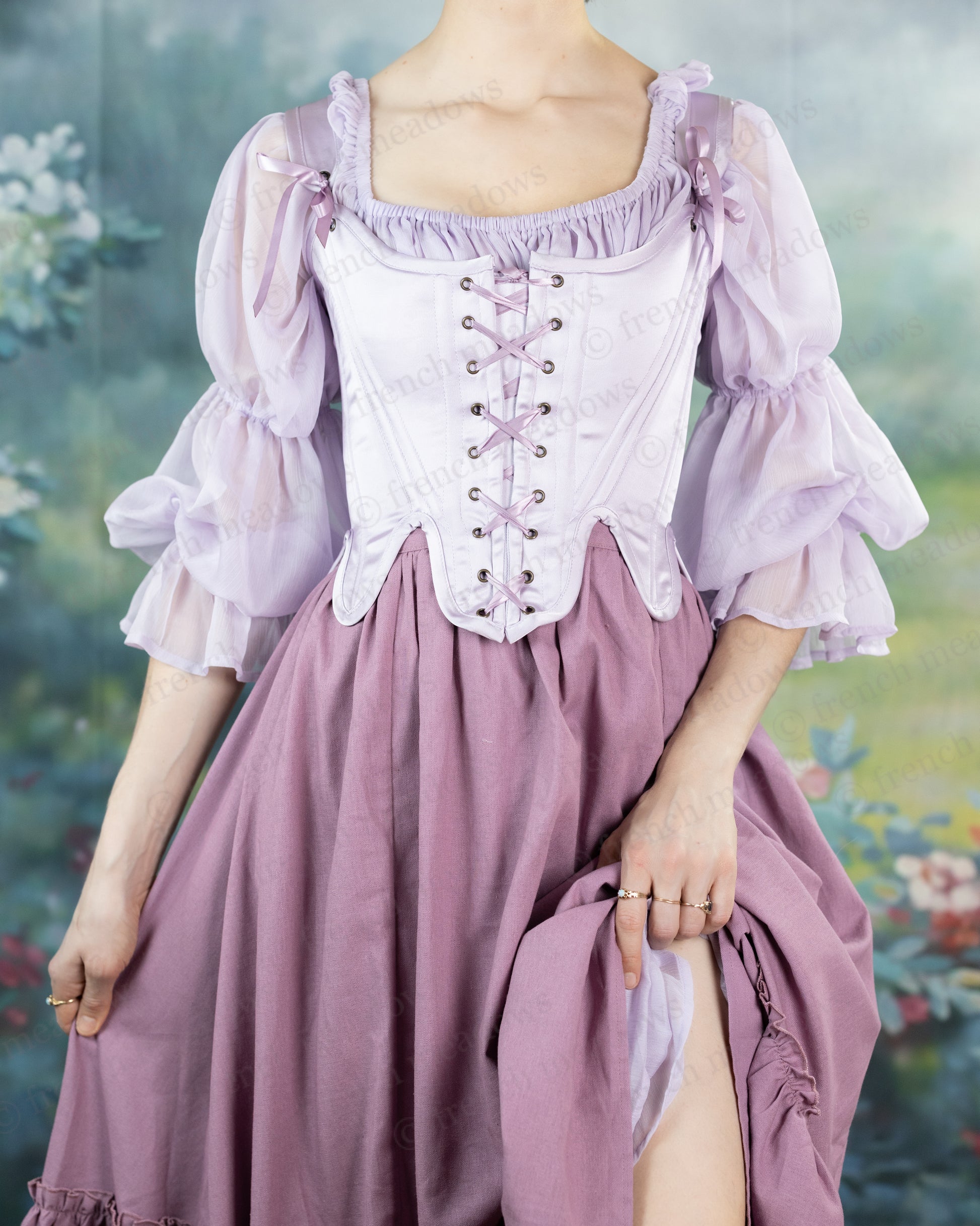 Lilac Satin 18th Century Stays with ruffled sleeves, front lacing corset bodice, and flowing mauve skirt in romantic garden setting