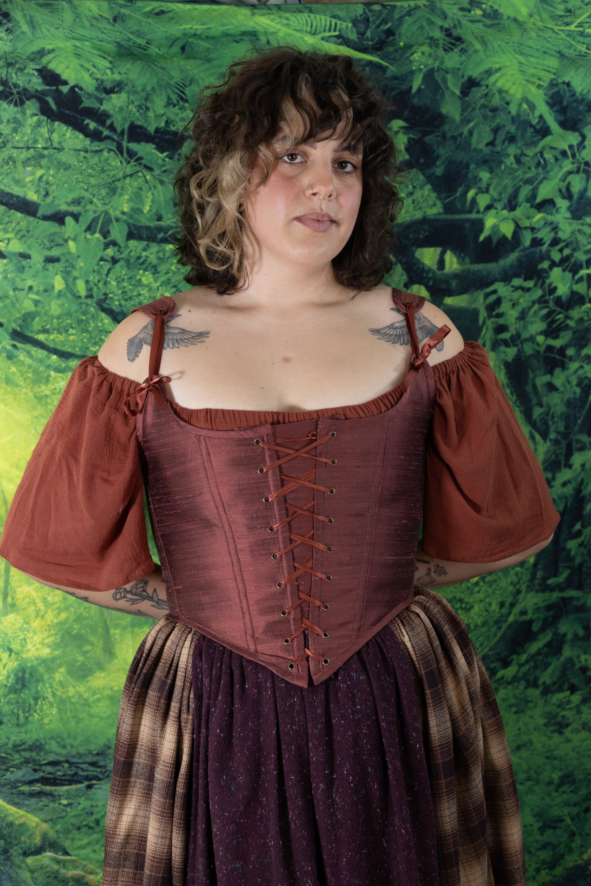 Woman with curly hair wearing Handmade Mary Sanderson Silk Corset in reddish-brown over a puff-sleeve blouse outdoors