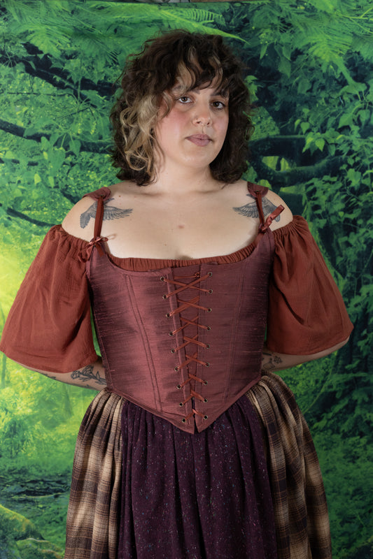 Woman with curly hair wearing Handmade Mary Sanderson Silk Corset in reddish-brown over a puff-sleeve blouse outdoors