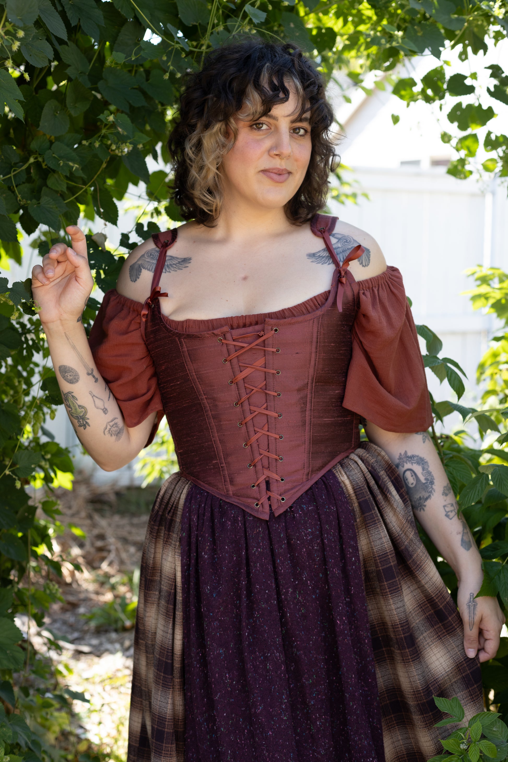 Woman wearing a Handmade Mary Sanderson Silk Corset with off-shoulder sleeves and a patterned skirt outdoors
