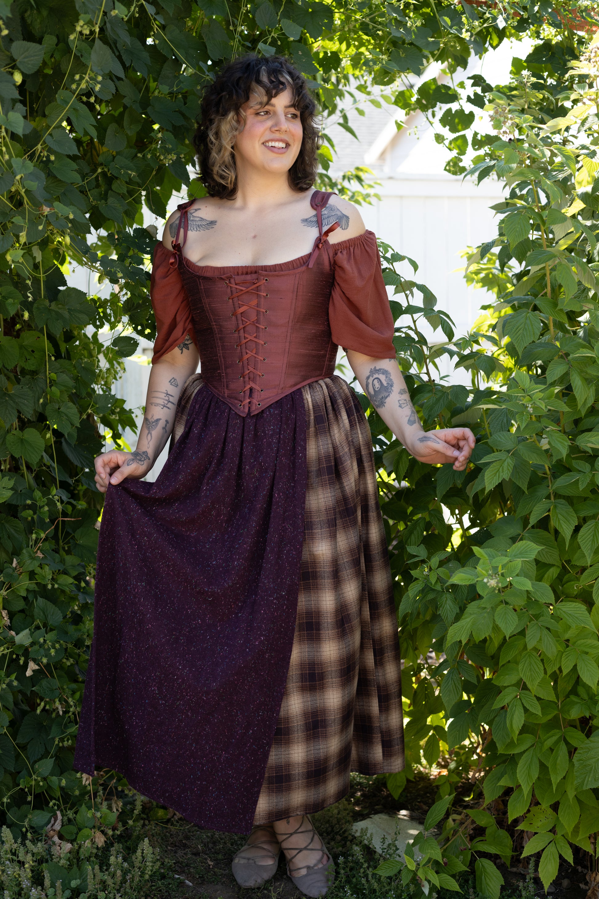 Woman wearing a Handmade Mary Sanderson Silk Corset with off-shoulder sleeves standing in a garden setting