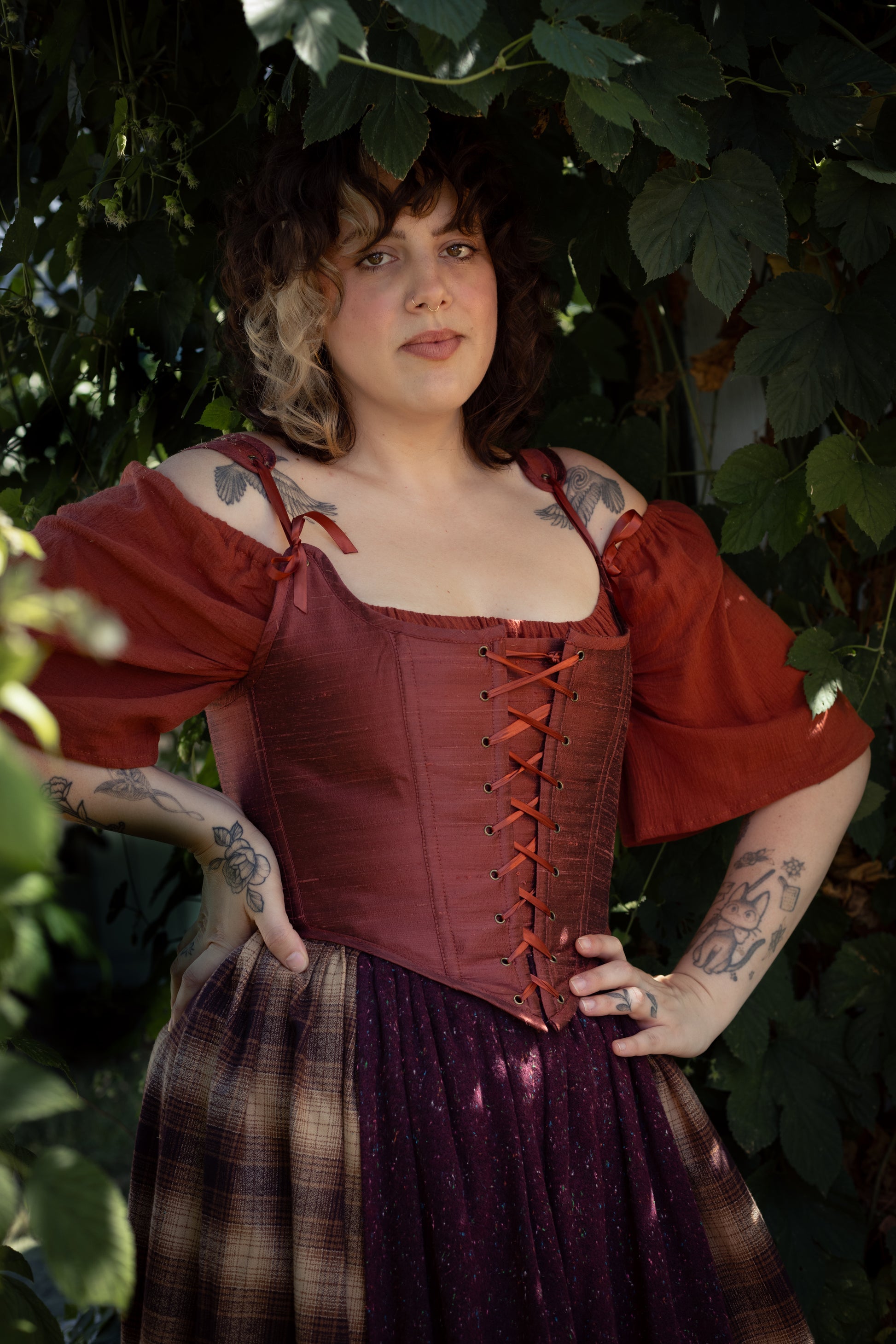 Woman wearing a Handmade Mary Sanderson Silk Corset with puff sleeves standing among leafy greenery