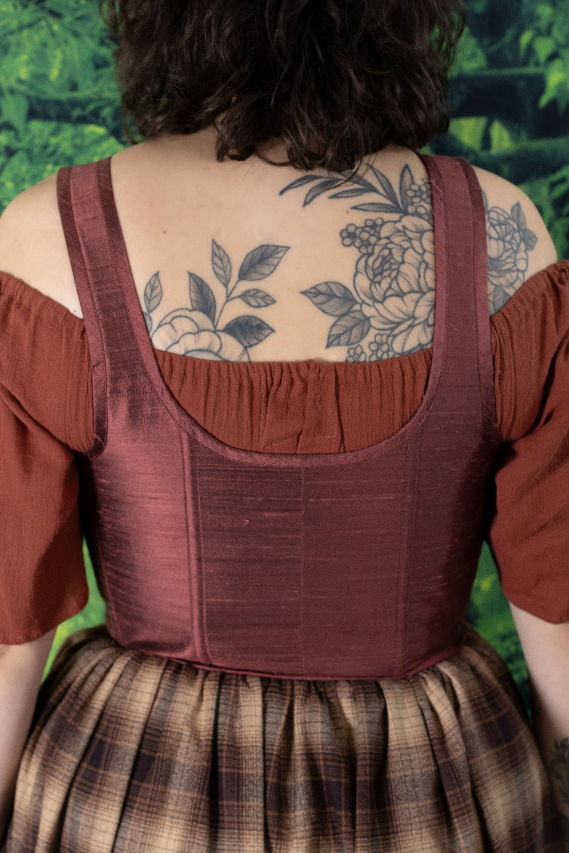 Back view of a person wearing Handmade Mary Sanderson Silk Corset over rust-colored blouse and plaid skirt.
