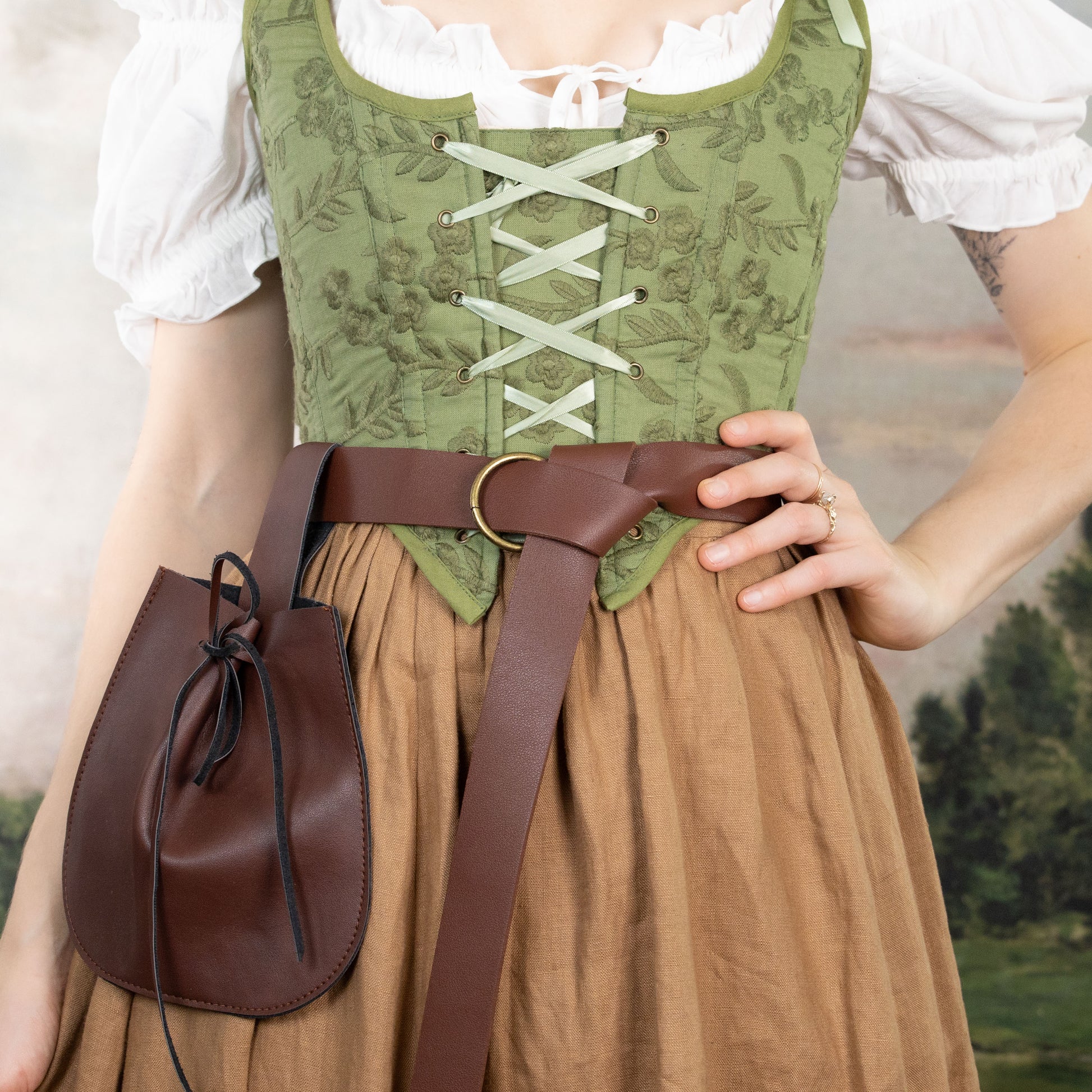 Woman wearing Handmade Moss Green Embroidered Floral Corset with white blouse and brown skirt, accessorized with leather belt pouch