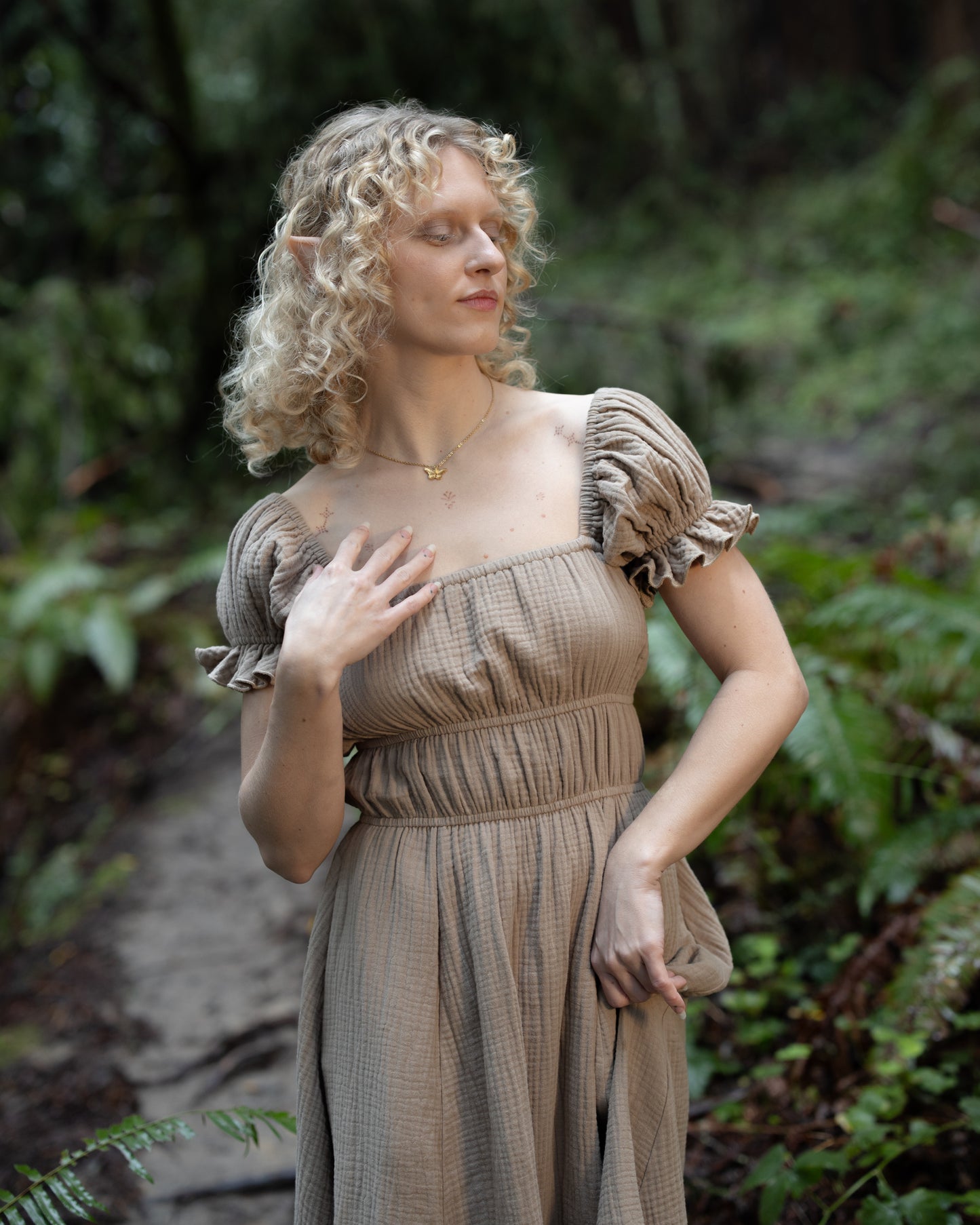 Woman wearing a Brown Milkmaid Dress with puff sleeves standing in a forest with eyes closed and curly hair