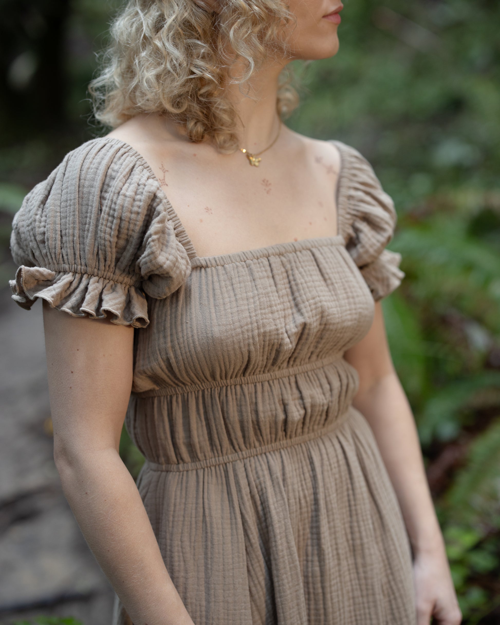 Woman wearing a Brown Milkmaid Dress with puffed sleeves and smocked bodice in an outdoor natural setting