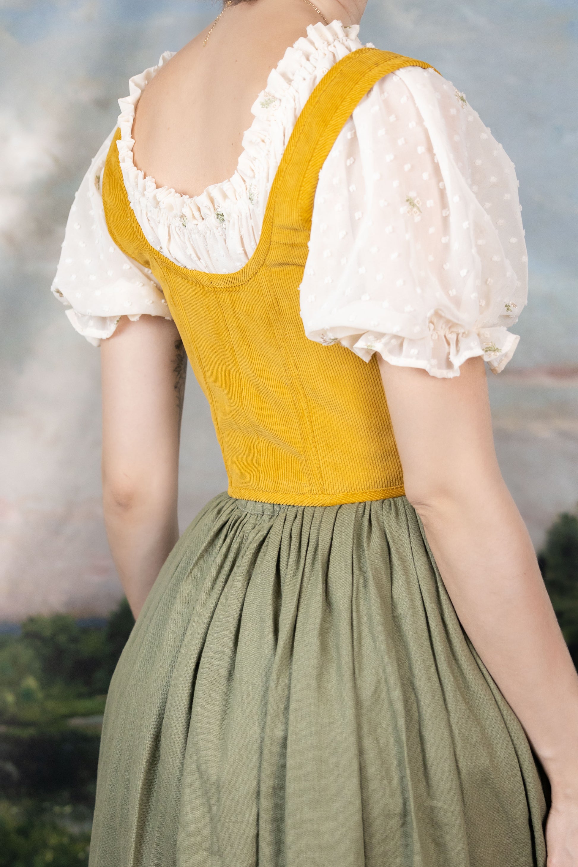 Back view of a person wearing a Handmade Mustard Corduroy Renaissance Corset with a white puff sleeve blouse and green skirt