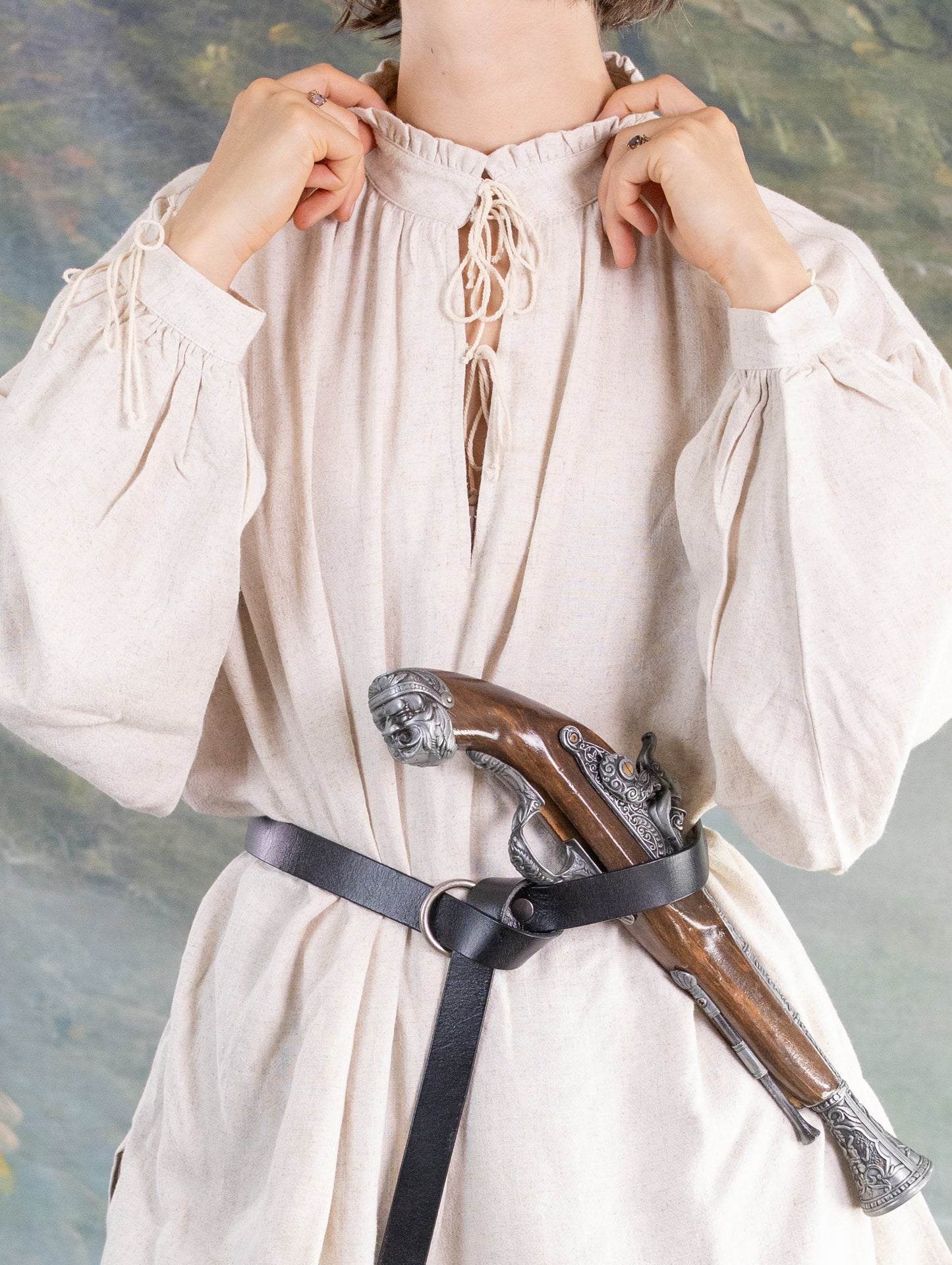 Person wearing a loose linen Borgia Shirt with puffed sleeves and a leather belt holding a vintage pistol.