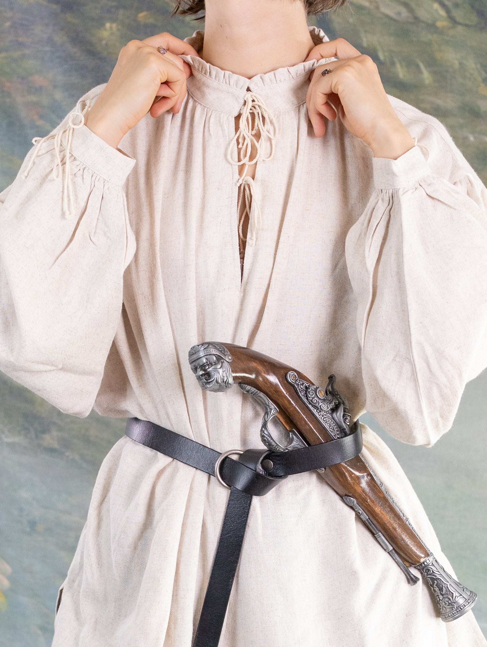 Person wearing a loose linen Borgia Shirt with puffed sleeves and a leather belt holding a vintage pistol.