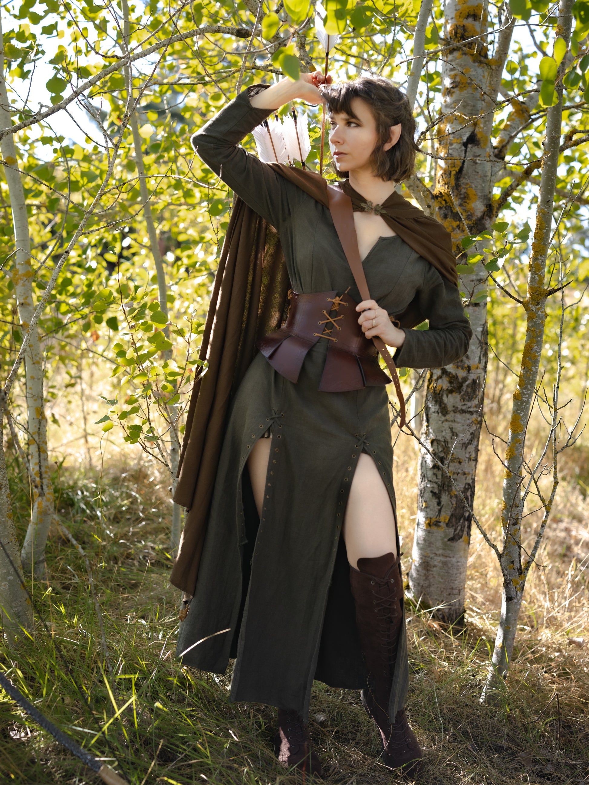 Olive Green Viking Dress with laced front and side slits shown on model in sunlit forest setting with autumn leaves