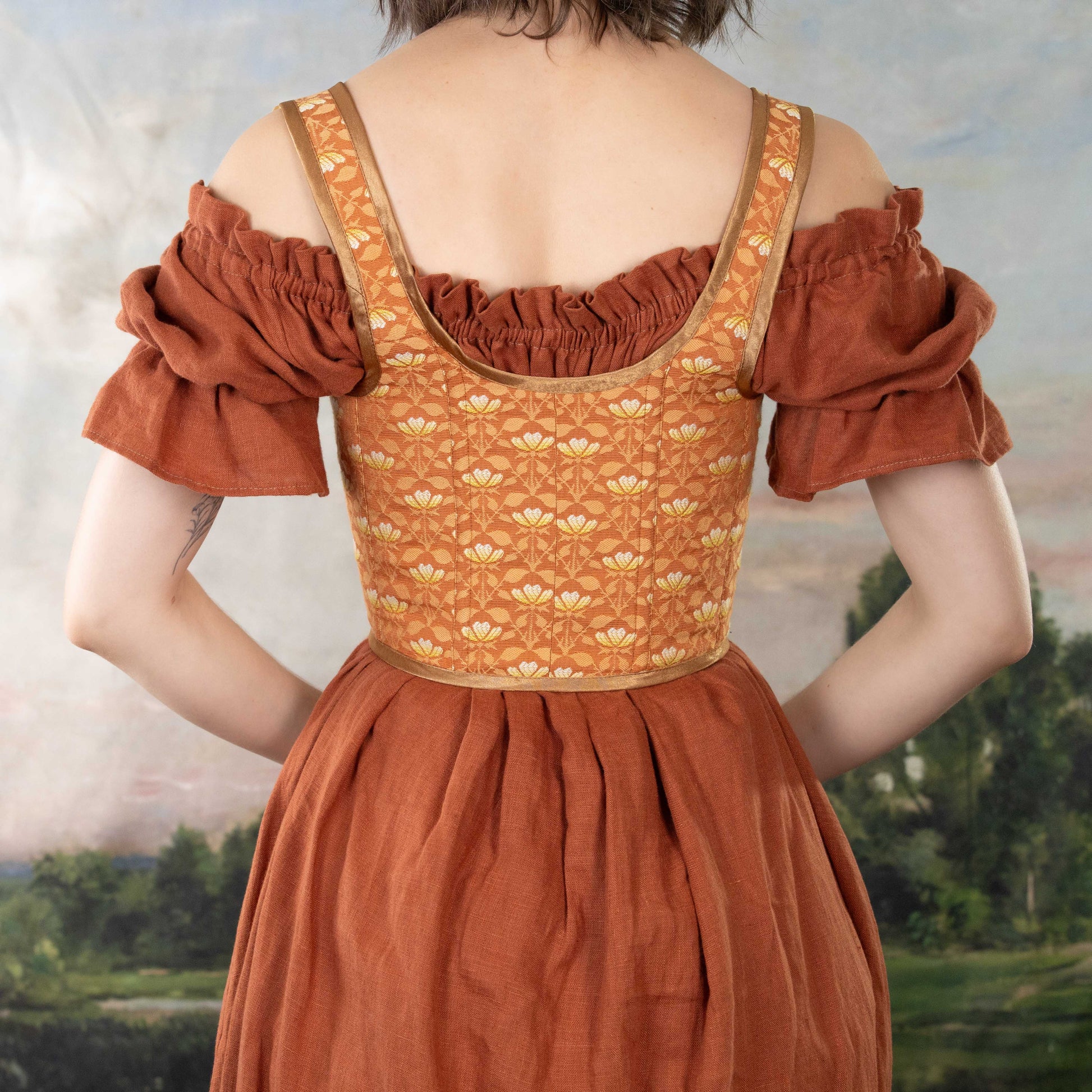 Woman wearing Handmade Orange Floral Jacquard Corset over a rust-colored off-shoulder dress with a scenic background