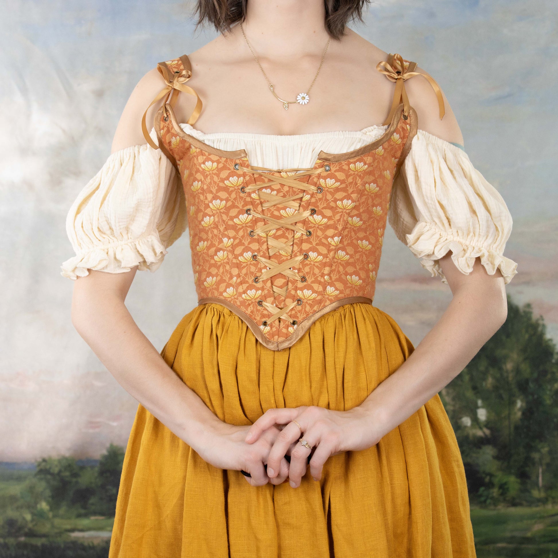 Woman wearing a Handmade Orange Floral Jacquard Corset over a cream blouse and mustard skirt, hands clasped in front
