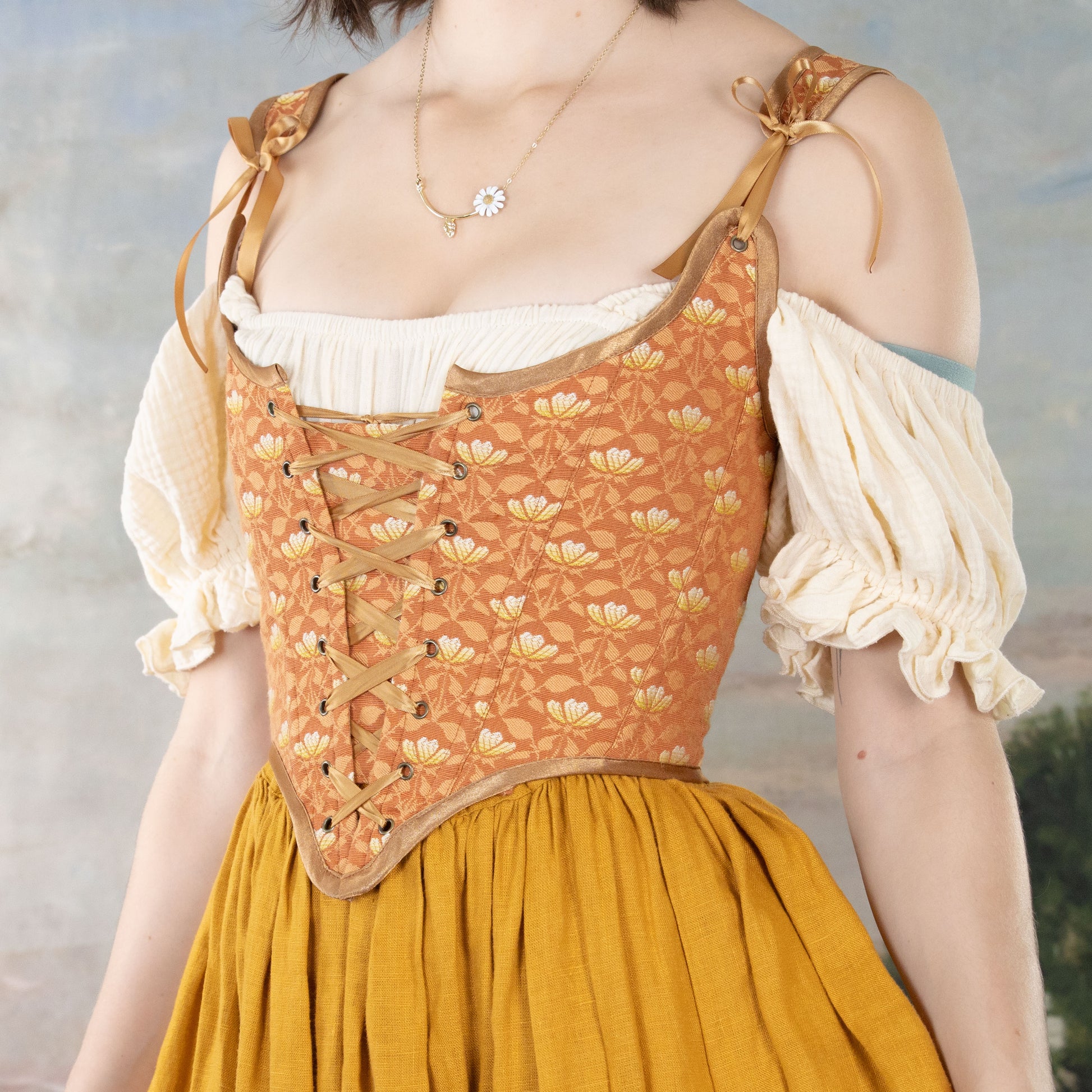 Woman wearing a Handmade Orange Floral Jacquard Corset with lace-up front over puffed sleeve blouse and mustard skirt