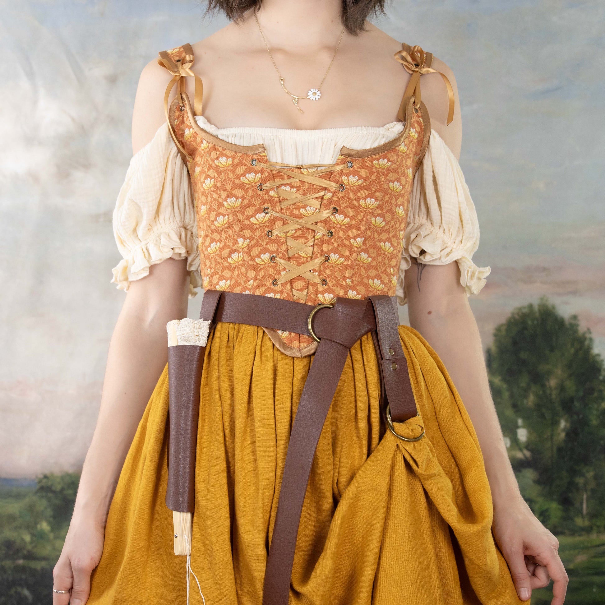 Woman wearing a Handmade Orange Floral Jacquard Corset with puffed sleeves, mustard skirt, and leather belt accessories