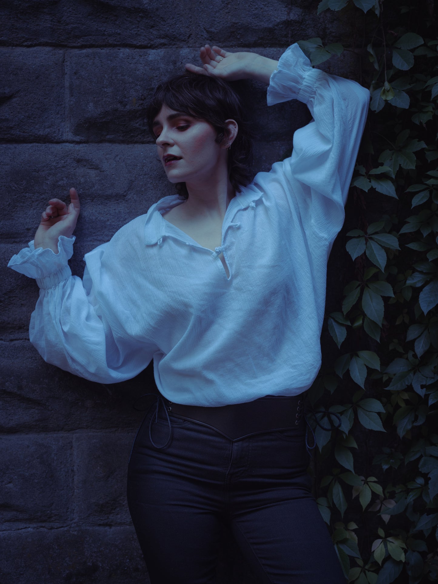 Woman wearing Darcy Shirt with billowing sleeves and knotted button neckline against stone wall background