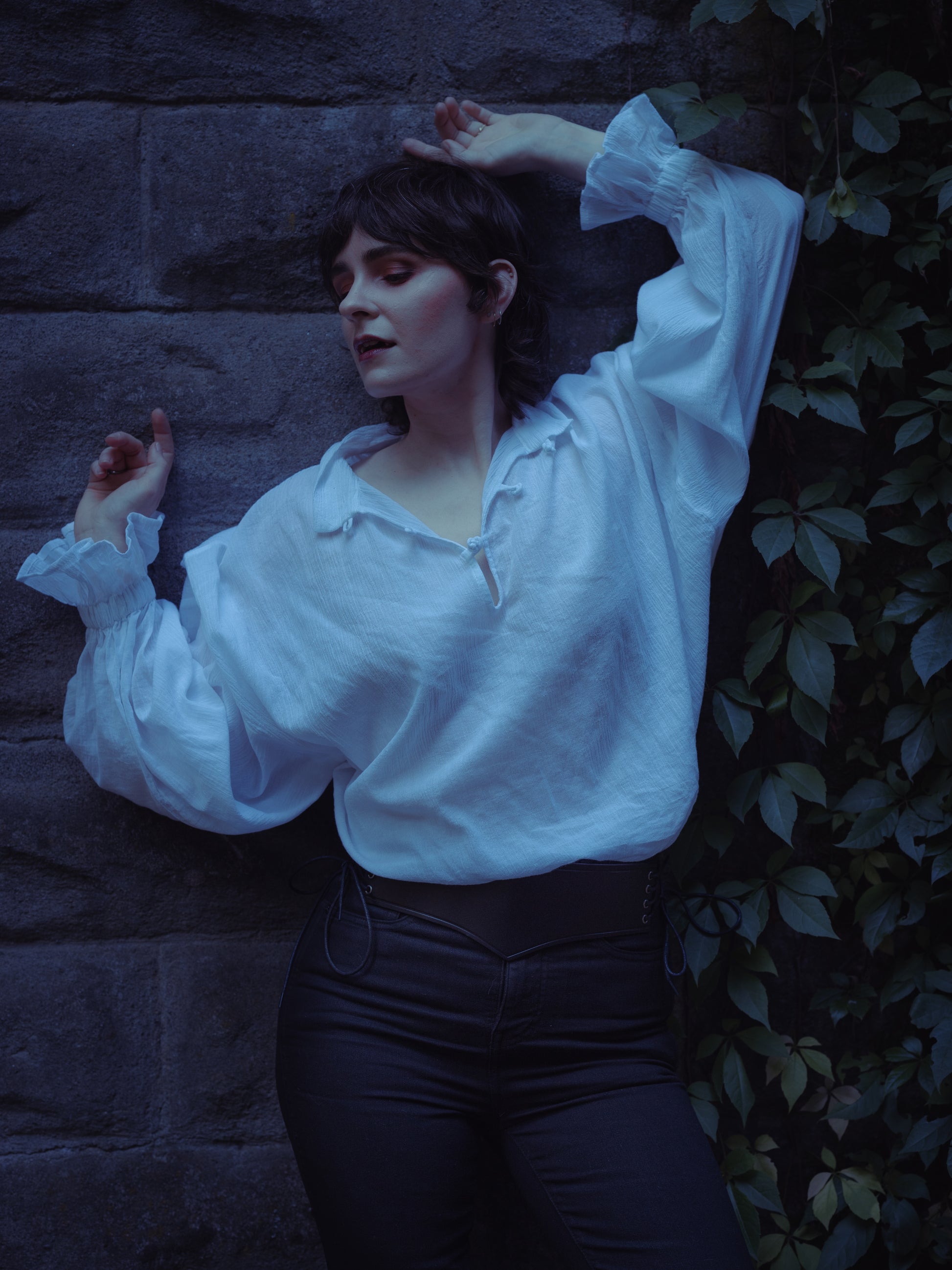 Woman wearing Darcy Shirt with billowing sleeves and knotted button neckline against stone wall background
