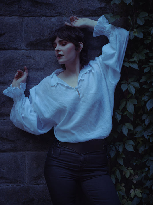 Woman wearing Darcy Shirt with billowing sleeves and knotted button neckline against stone wall background