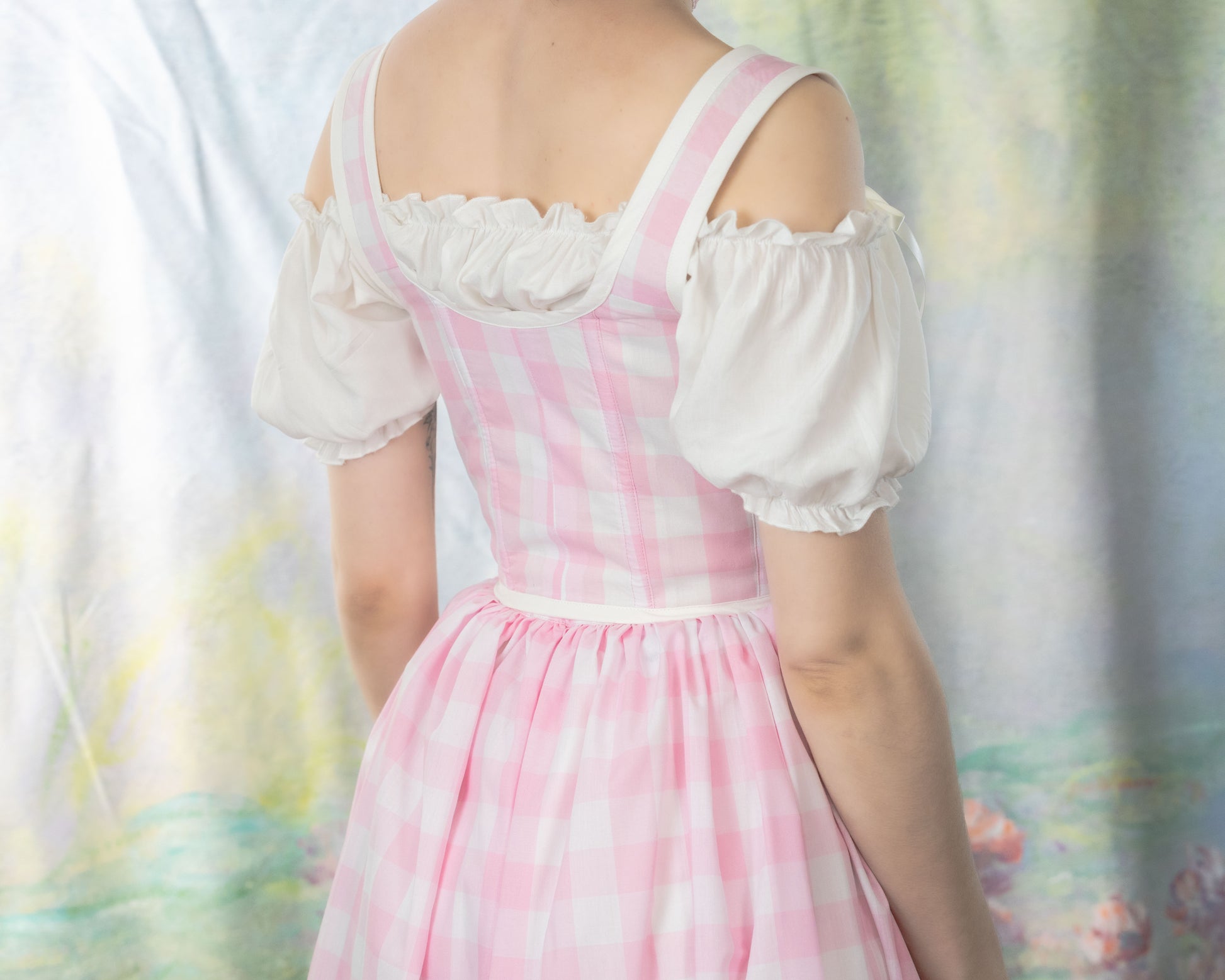 Back view of a Handmade Pink Gingham Corset worn with a white puff sleeve blouse in soft lighting