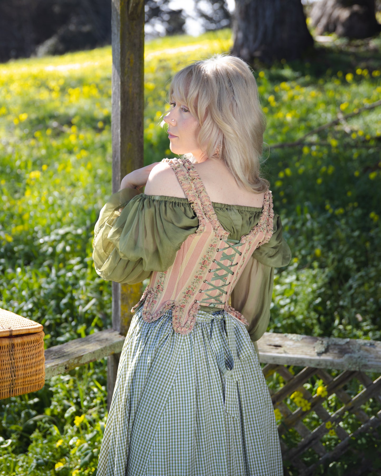 Woman wearing Rococo Pink 18th Century Stays with green blouse and checkered skirt in a sunny garden setting