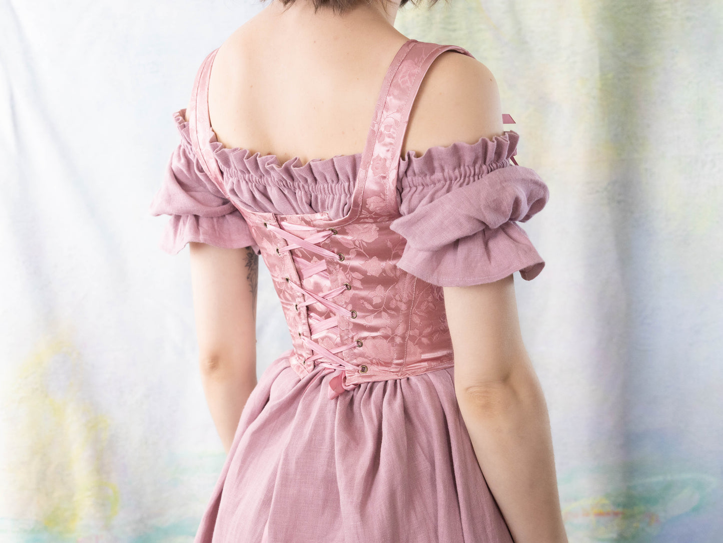 Back view of a woman wearing Handmade Pink Floral Satin Sarah Sanderson Stays with lace-up corset and ruffled sleeves