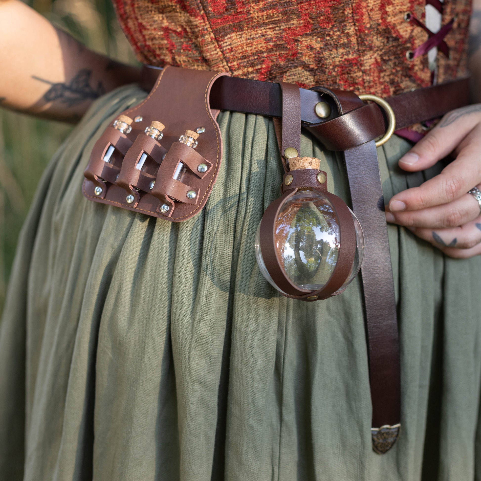 Person wearing Potion Bottle -- slightly damaged *Final Sale* attached to leather belt over green skirt and textured top