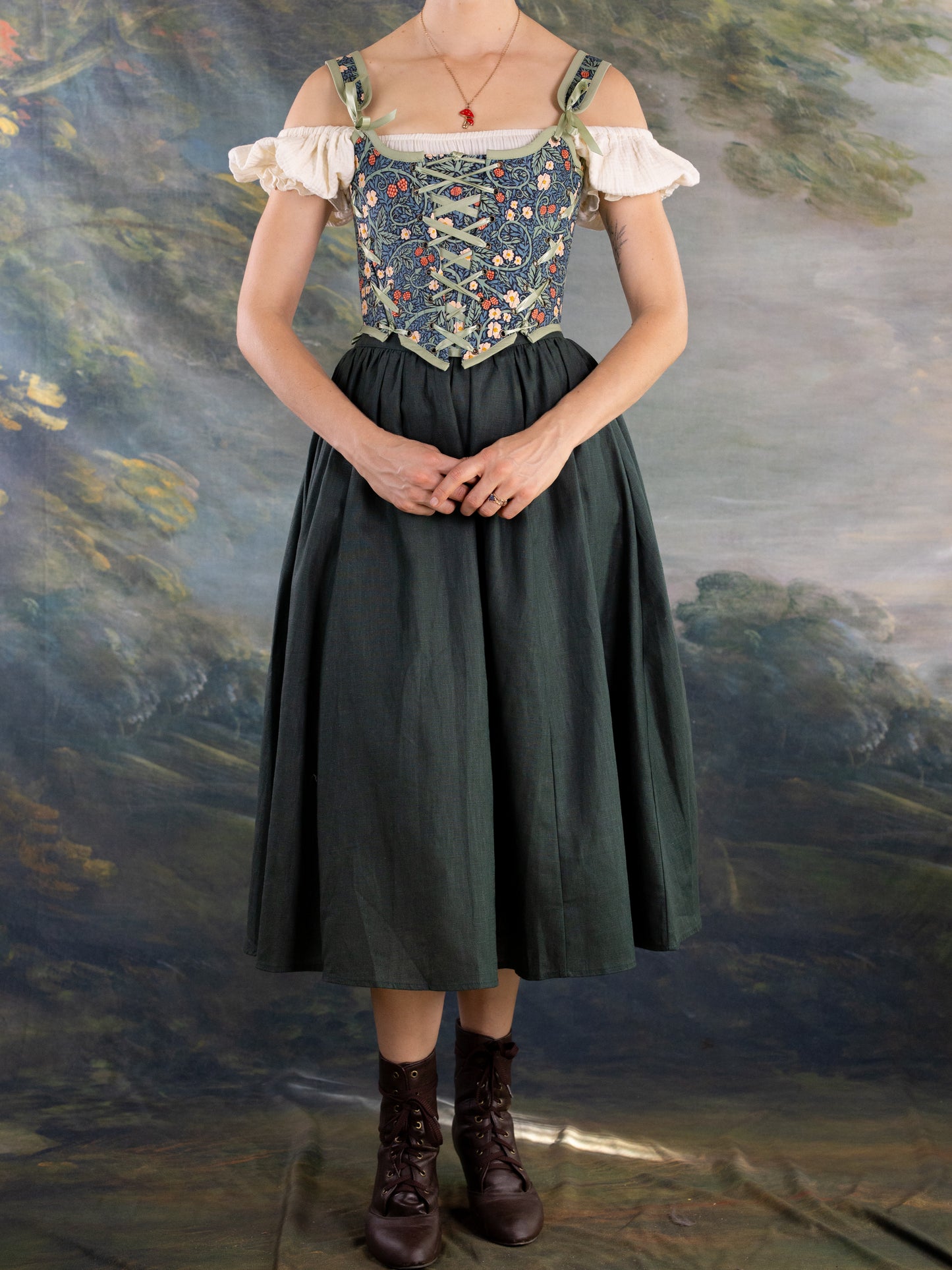 Woman wearing a floral corset style Raspberry Vines Princess Stays over a white blouse and dark skirt against painted backdrop