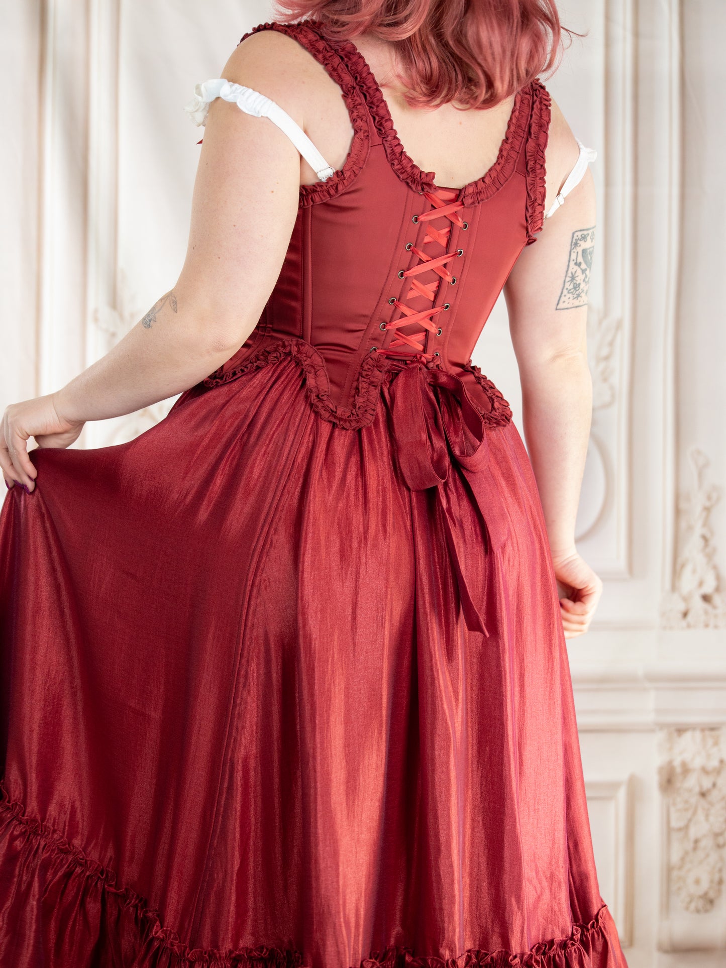 Back view of a woman wearing Red Satin 18th Century Stays with ruffled trim and lace-up back design.