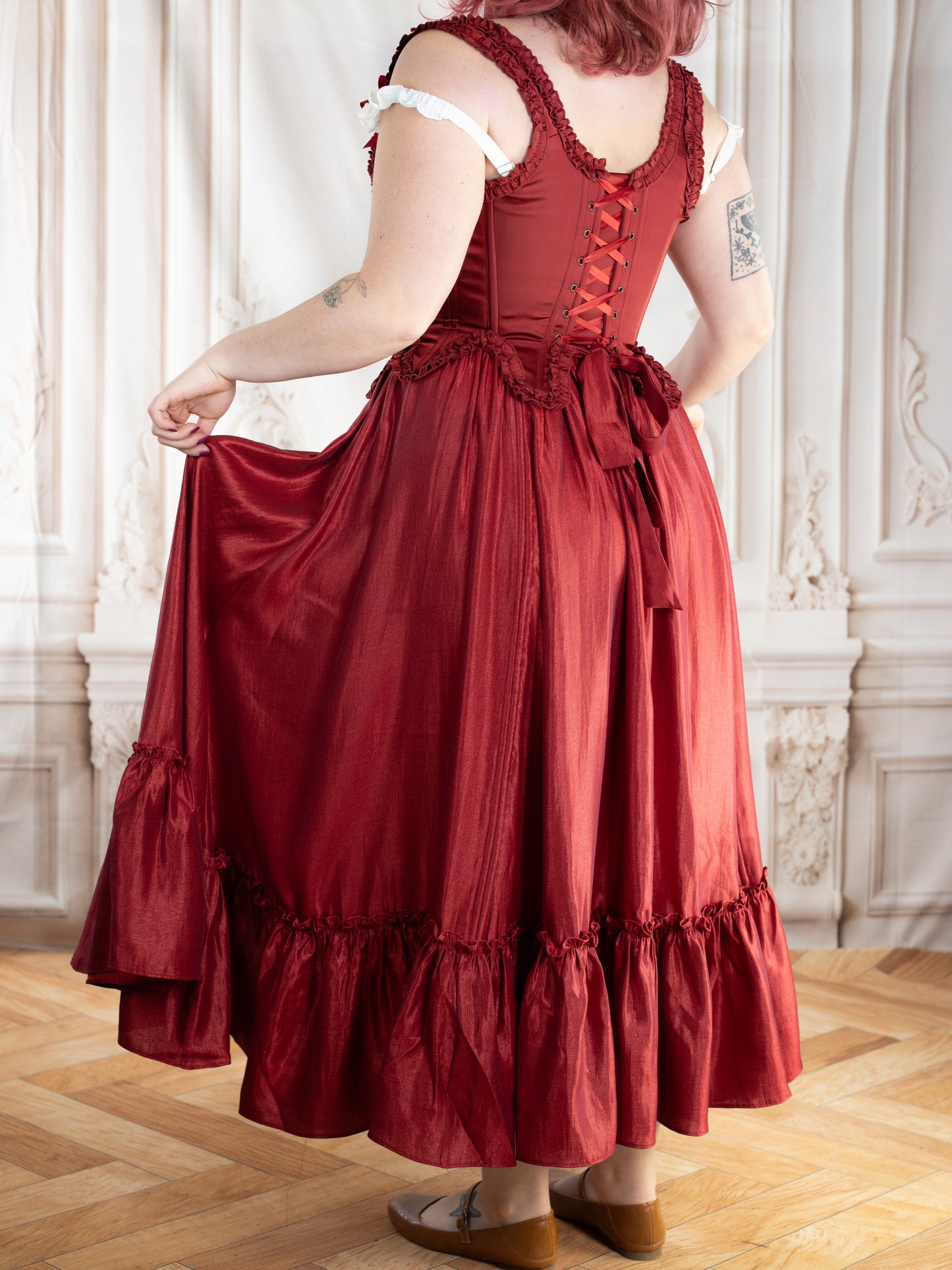 Back view of a woman wearing Red Satin 18th Century Stays with elegant ruffle trims and ribbon lacing.