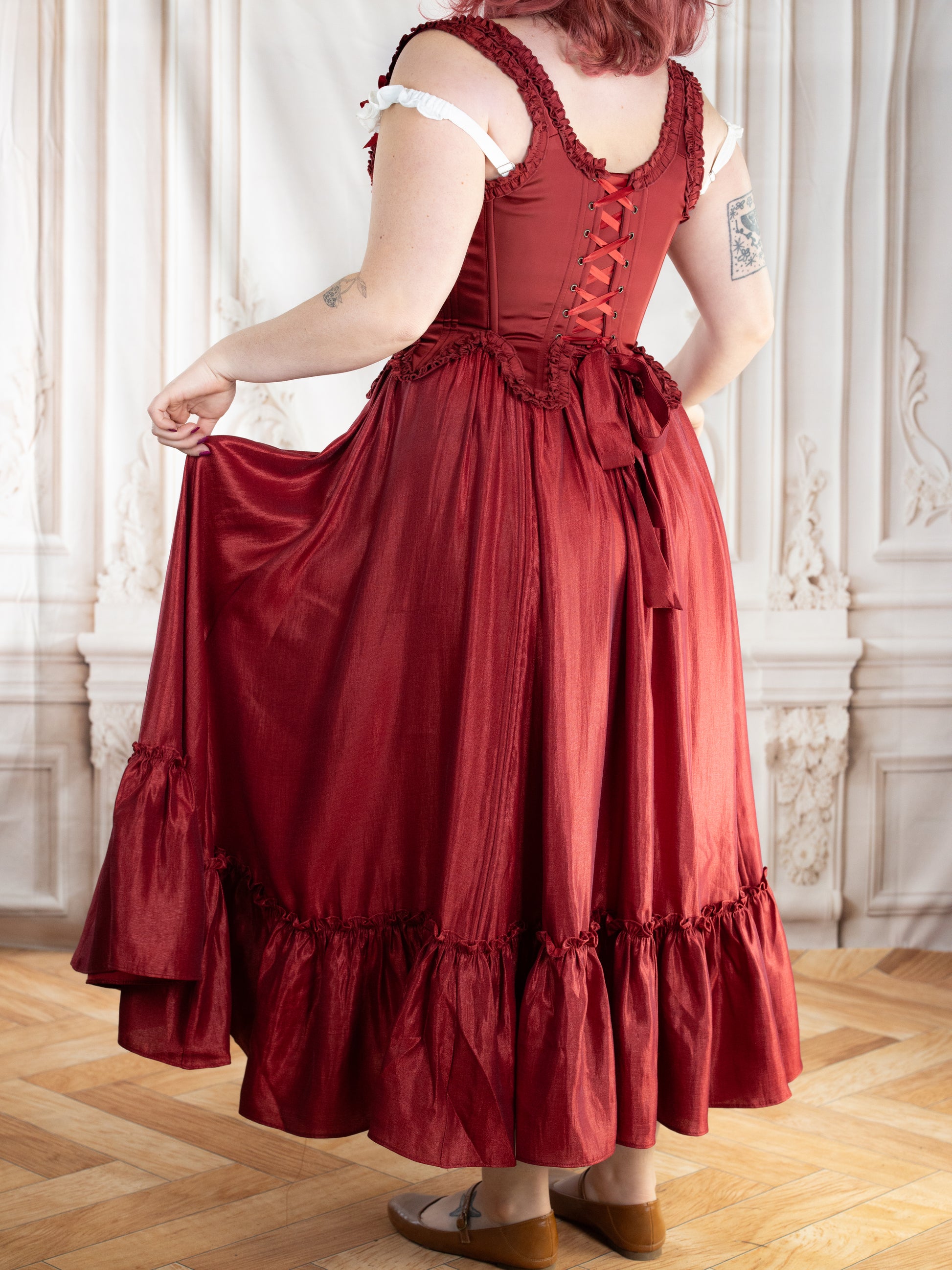 Back view of a woman wearing Red Satin 18th Century Stays with elegant ruffle trims and ribbon lacing.