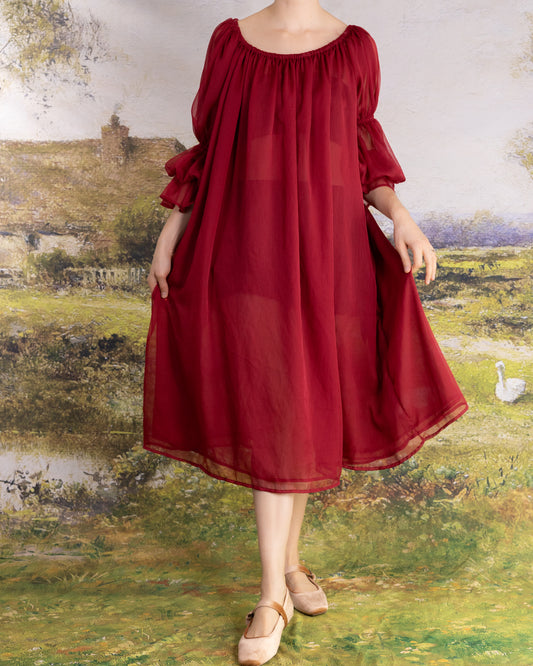 Woman wearing flowing red chiffon dress with puffed sleeves standing against painted countryside backdrop Red Chiffon Chemise