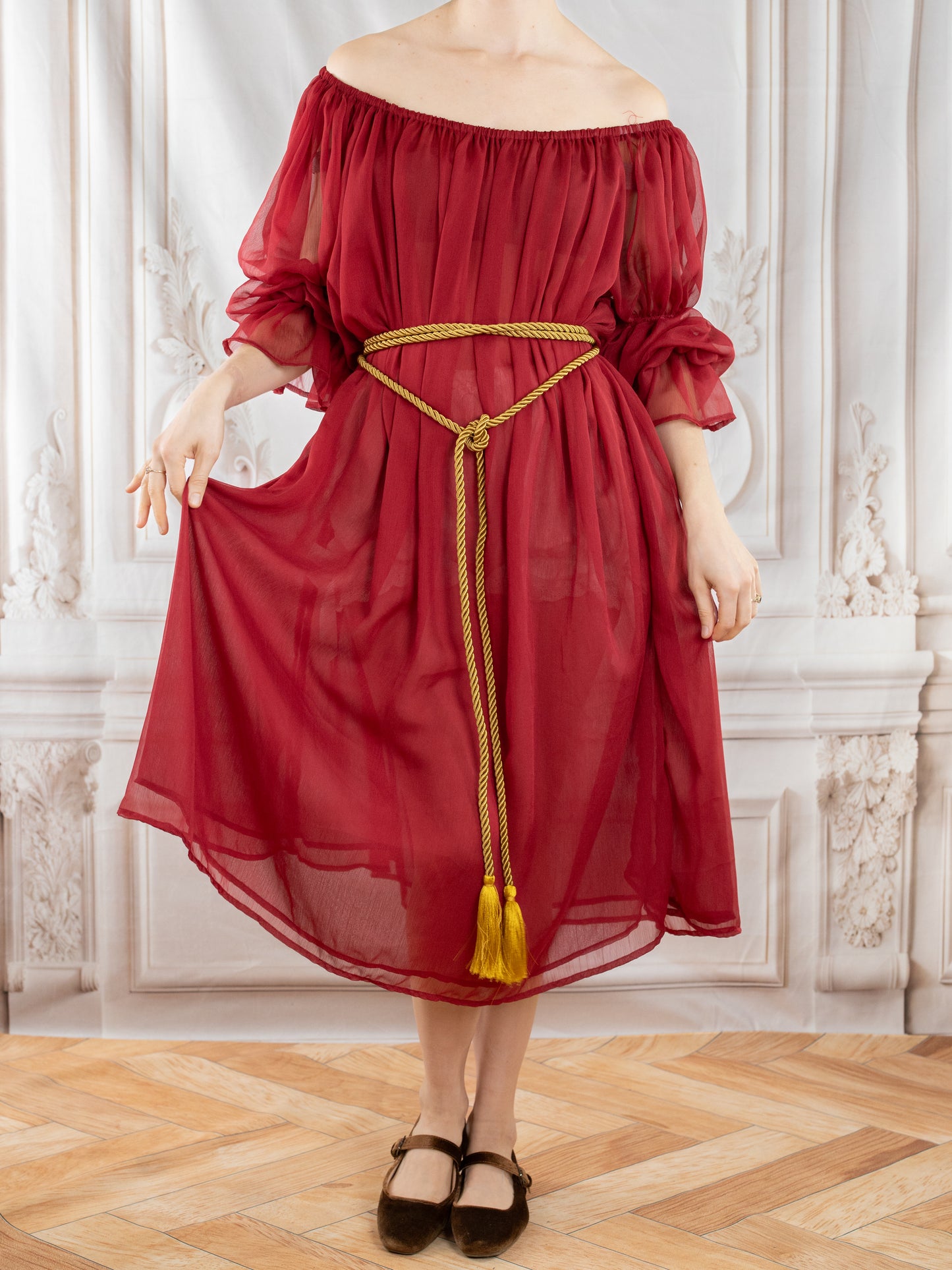 Woman wearing Red Chiffon Chemise with off-shoulder design and gold rope belt posing in elegant room