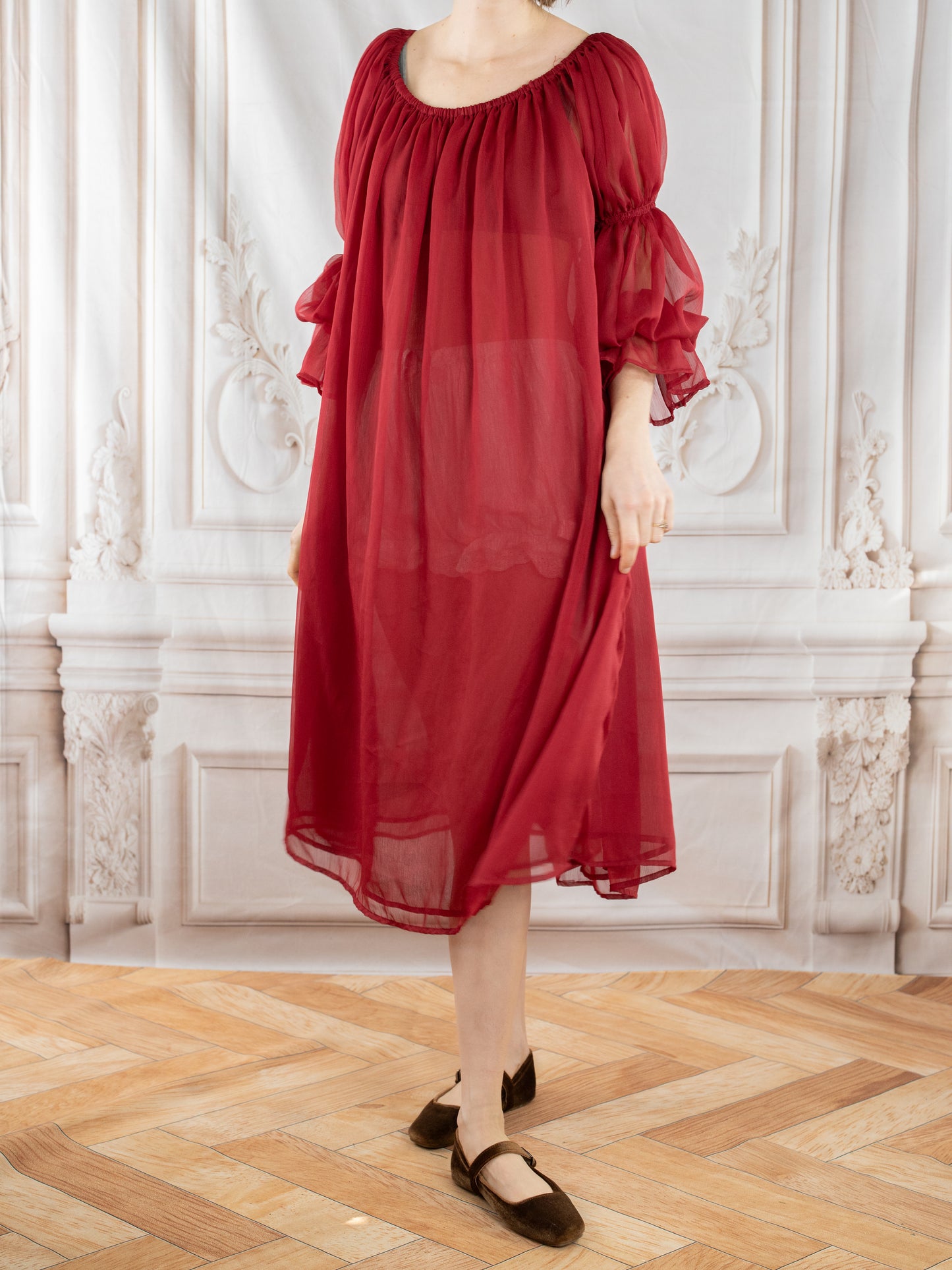 Woman wearing flowy Red Chiffon Chemise with puff sleeves standing in elegant room with wooden floor