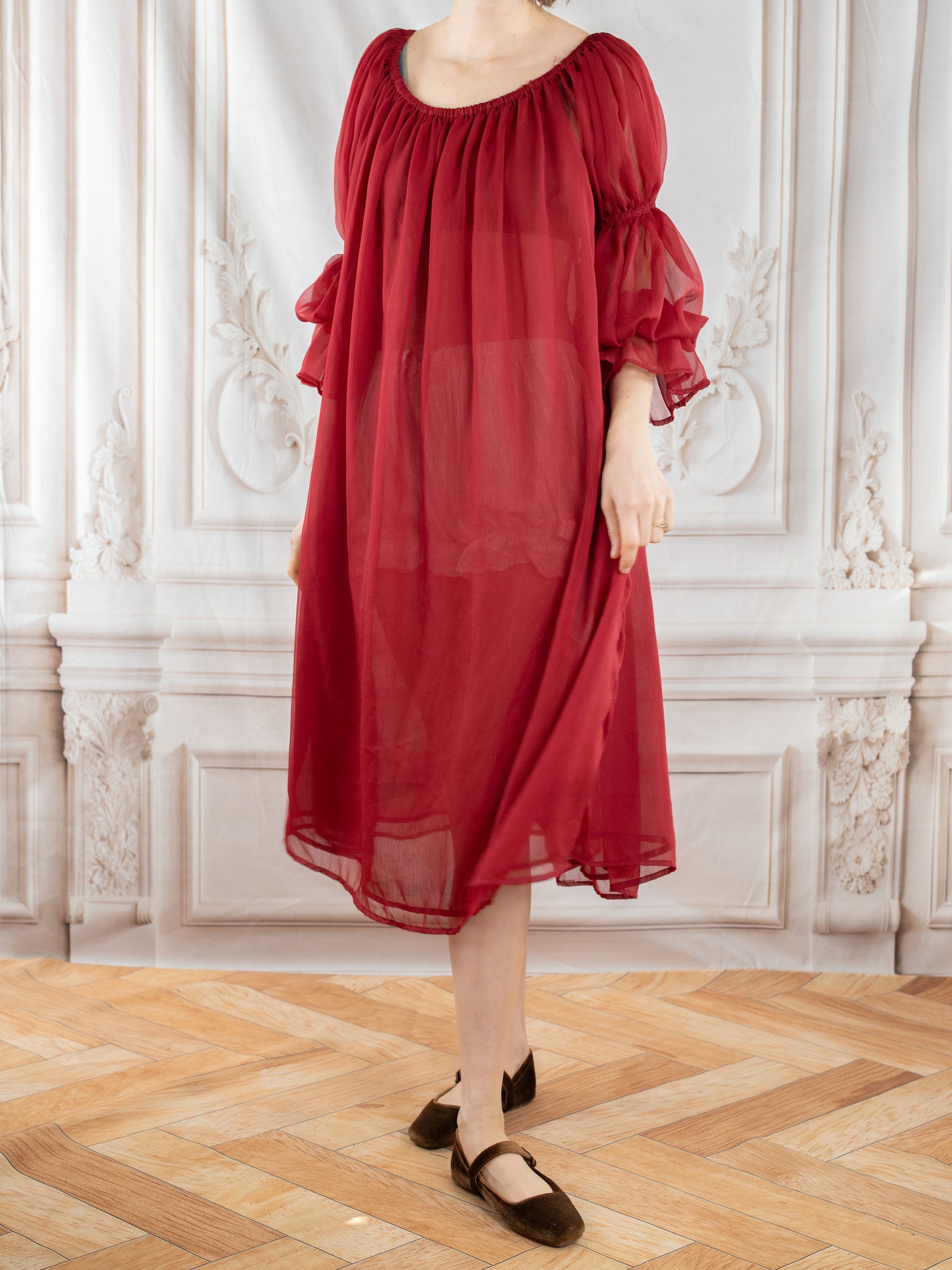 Woman wearing flowy Red Chiffon Chemise with puff sleeves standing in elegant room with wooden floor
