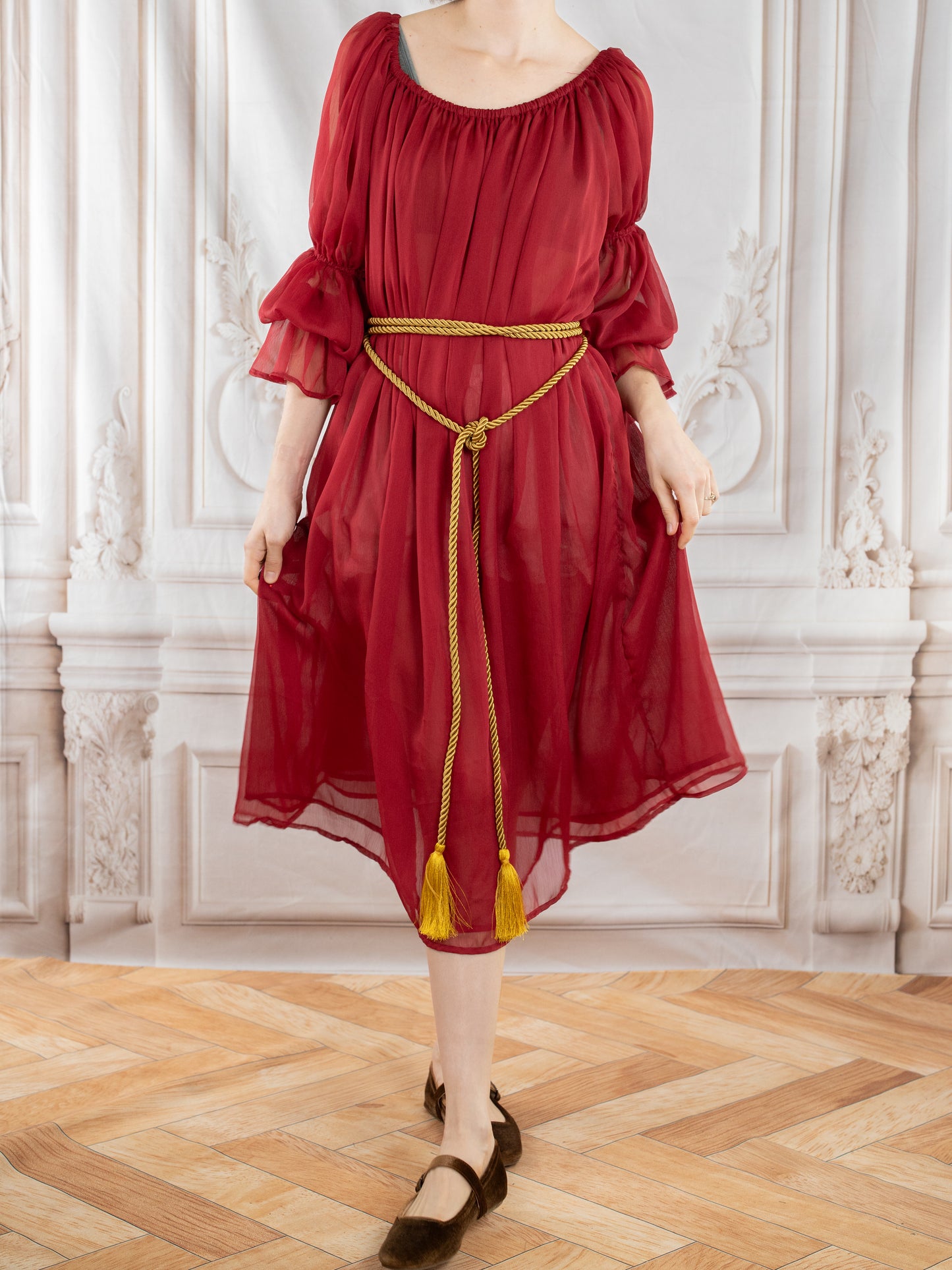Red Chiffon Chemise worn with a gold tasseled rope belt, showcasing sheer flowing fabric and puffed sleeves in a classic room setting.