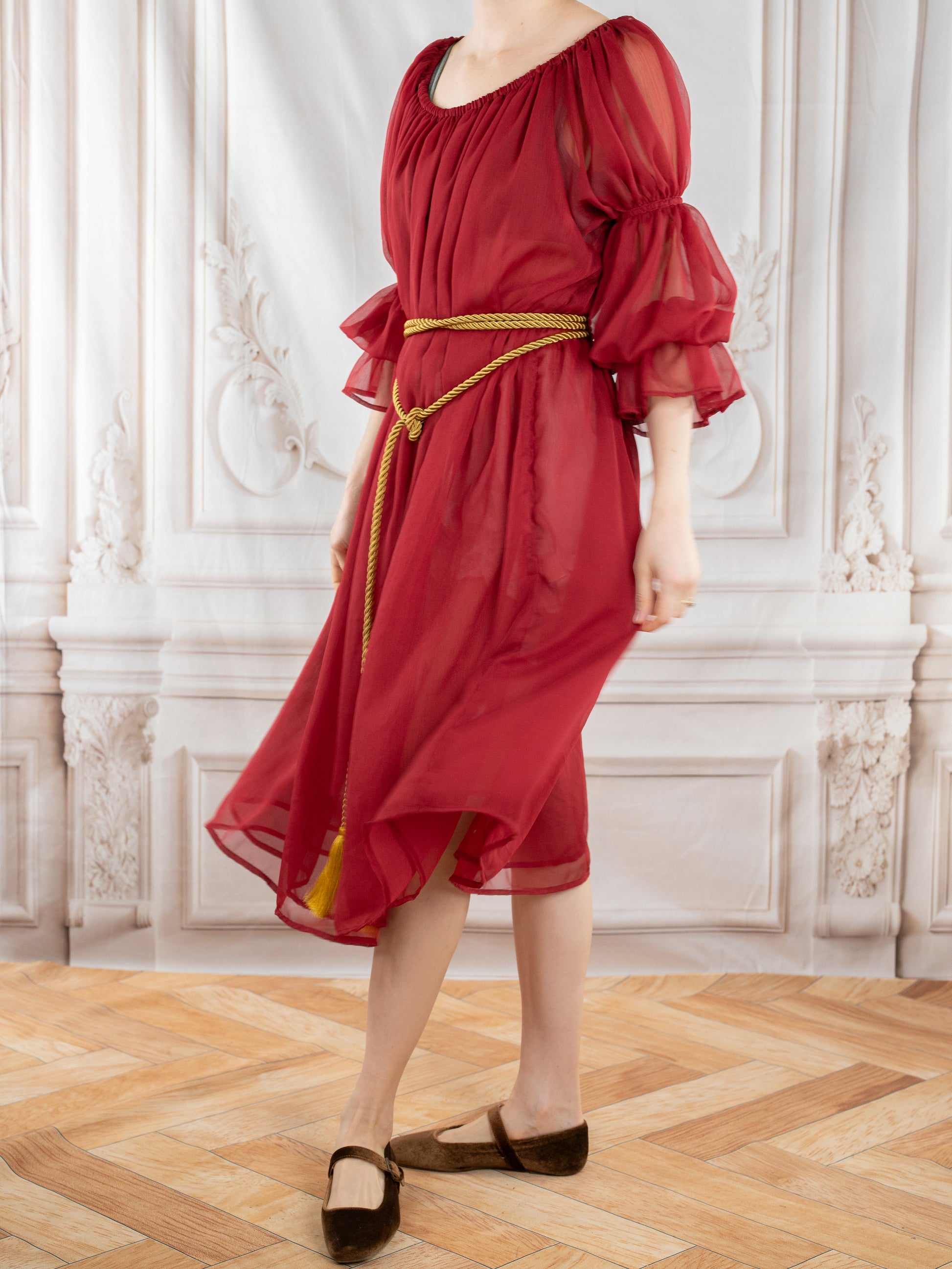 Woman wearing elegant Red Chiffon Chemise with sheer puff sleeves and gold rope belt standing indoors