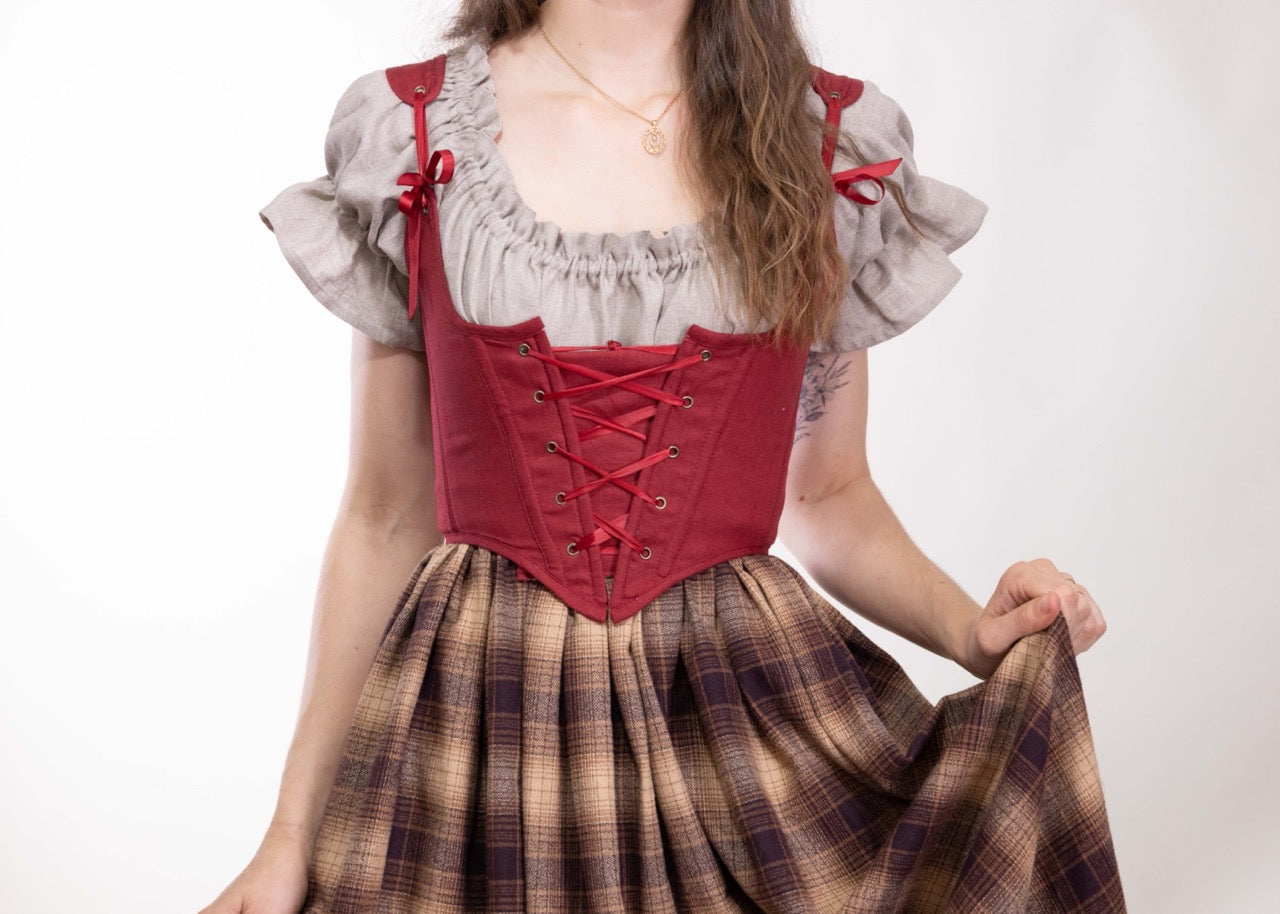 Woman wearing a Handmade Red Linen Corset over a ruffled blouse and plaid skirt, posed against white background