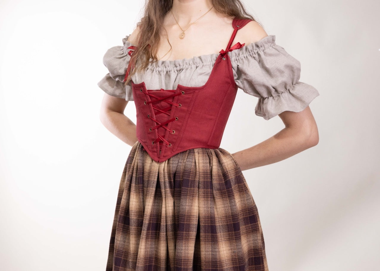 Woman wearing a Handmade Red Linen Corset over a puffed sleeve blouse and plaid skirt on a white background