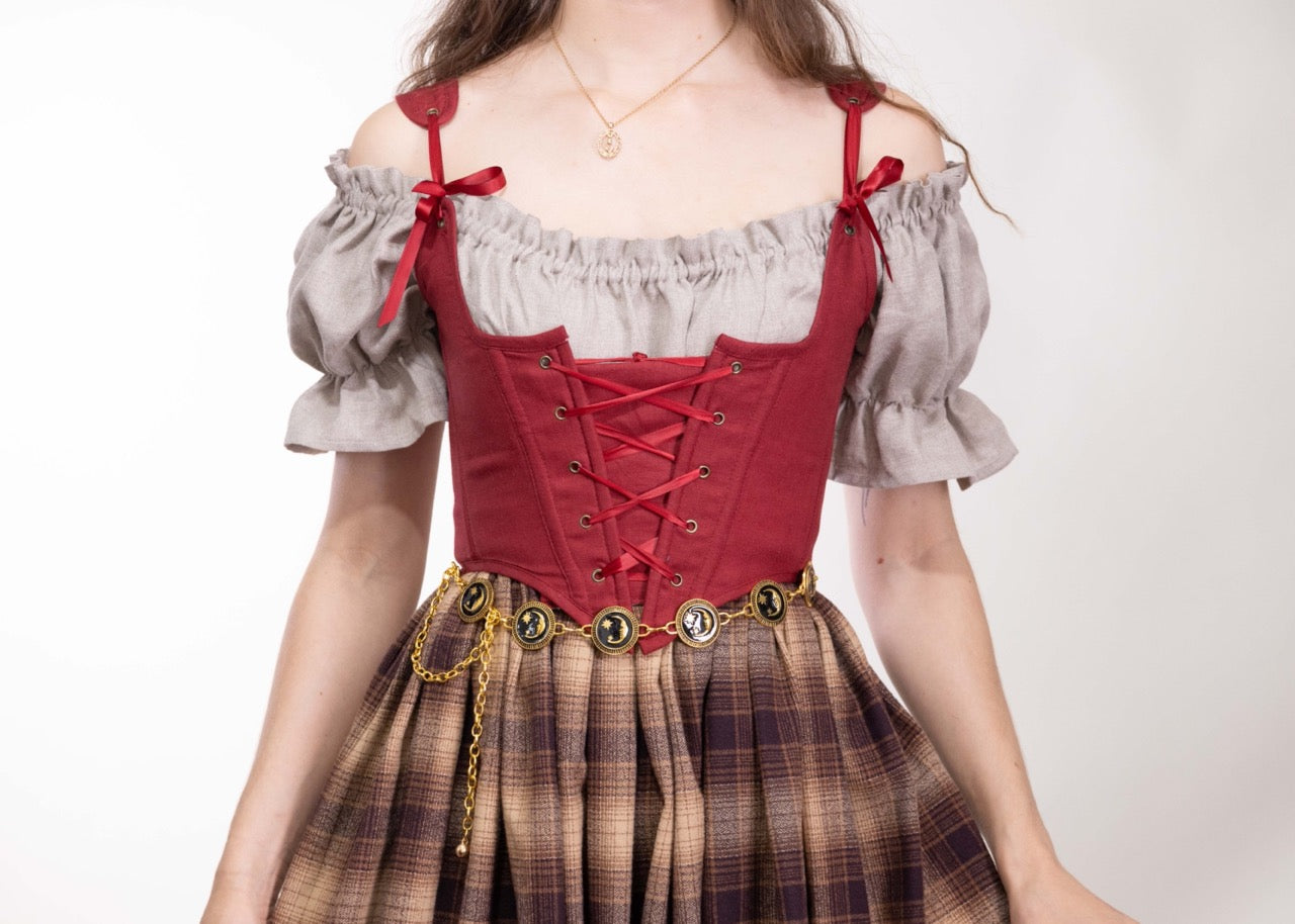 Woman wearing a Handmade Red Linen Corset over a beige blouse with puff sleeves and a plaid skirt with a decorative belt