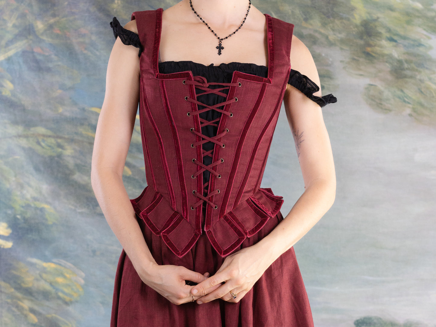 Woman wearing a structured Red Pirate Doublet with laced front and ruffled peplum detail against a painted backdrop