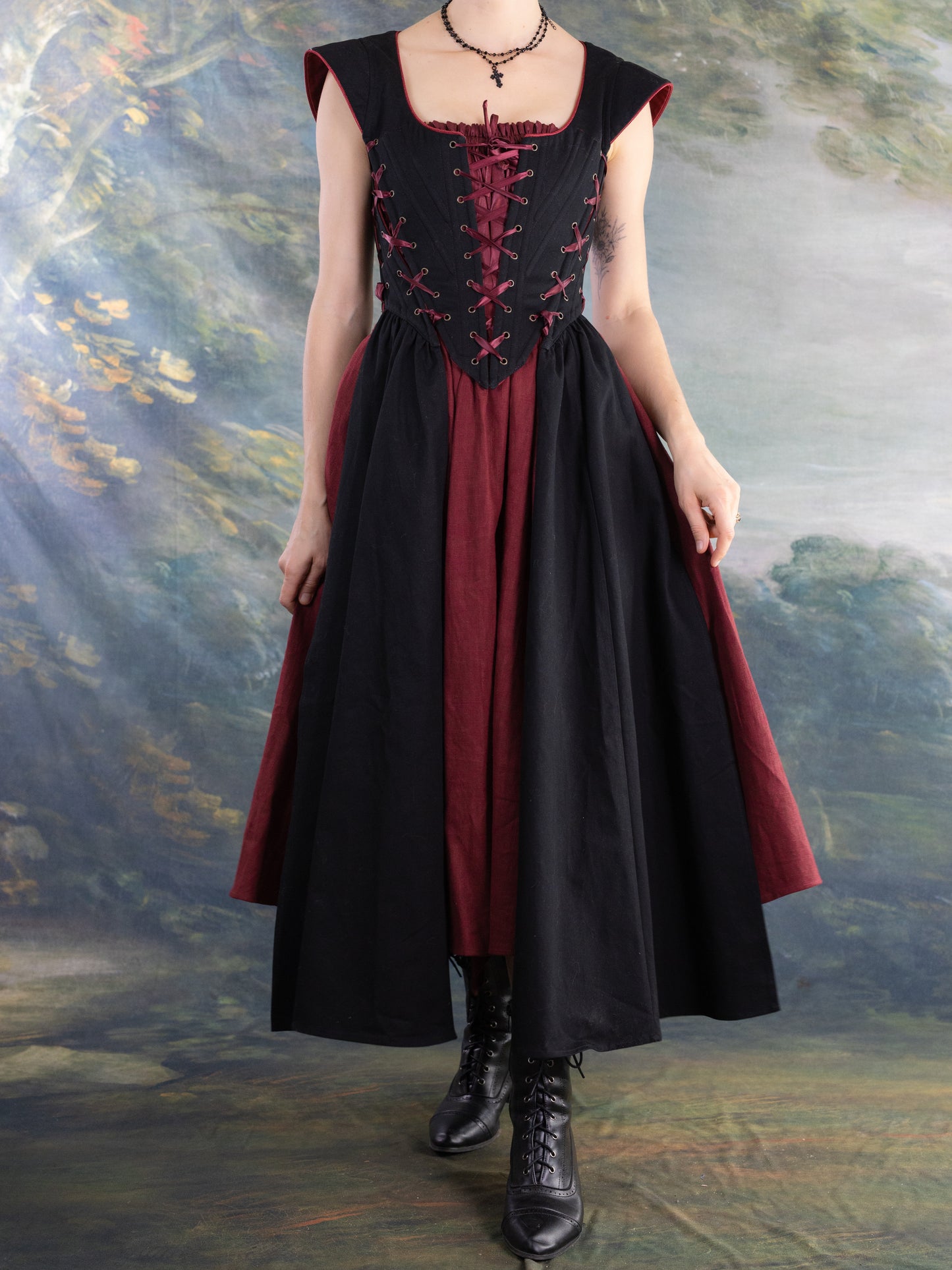 Woman wearing a Burgundy Ramie Midi Skirt styled for renaissance faire with black corset and boots in scenic backdrop