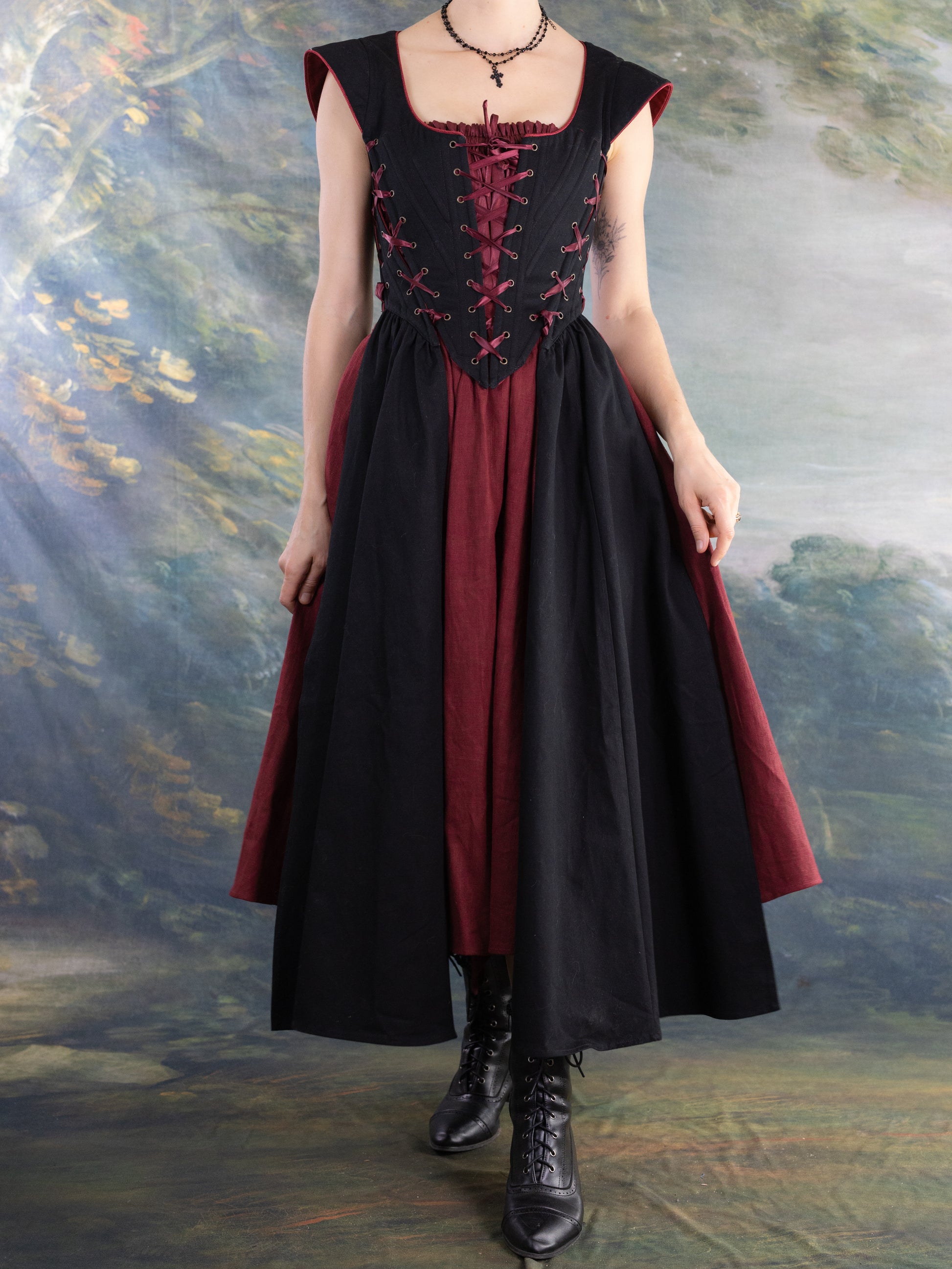Woman wearing a Burgundy Ramie Midi Skirt styled for renaissance faire with black corset and boots in scenic backdrop
