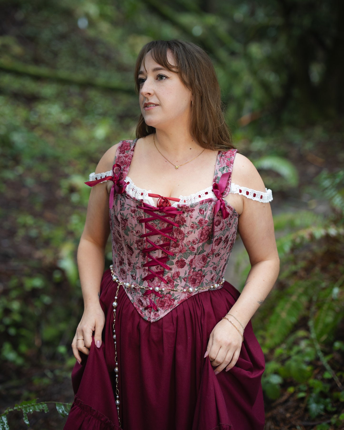 Woman wearing a Raspberry Rose Jacquard Corset with floral pattern and lace-up front in an outdoor natural setting