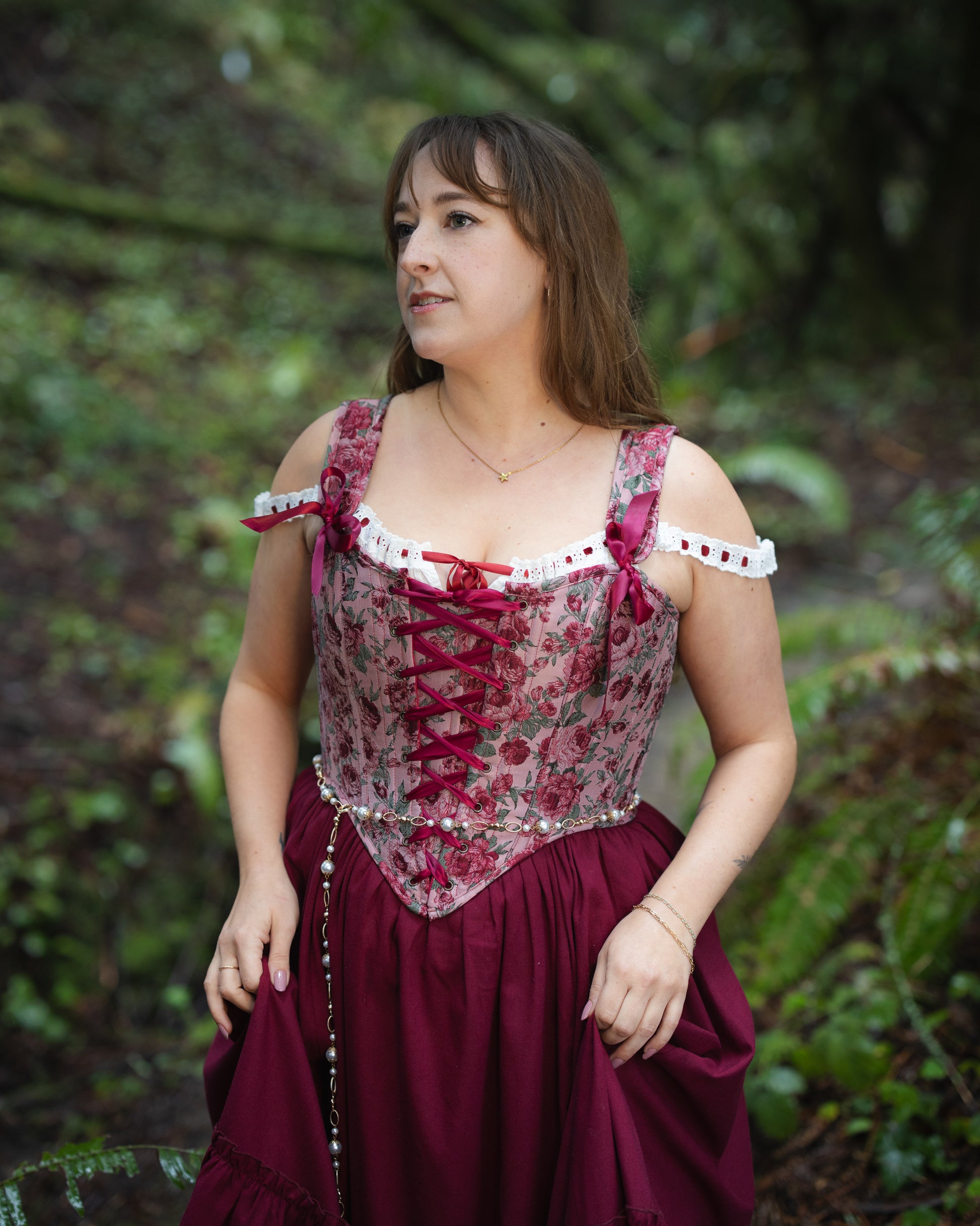 Woman wearing a Raspberry Rose Jacquard Corset with floral pattern and lace-up front in an outdoor natural setting