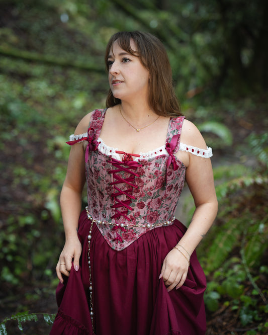 Woman wearing a Raspberry Rose Jacquard Corset with floral pattern and lace-up front in an outdoor natural setting